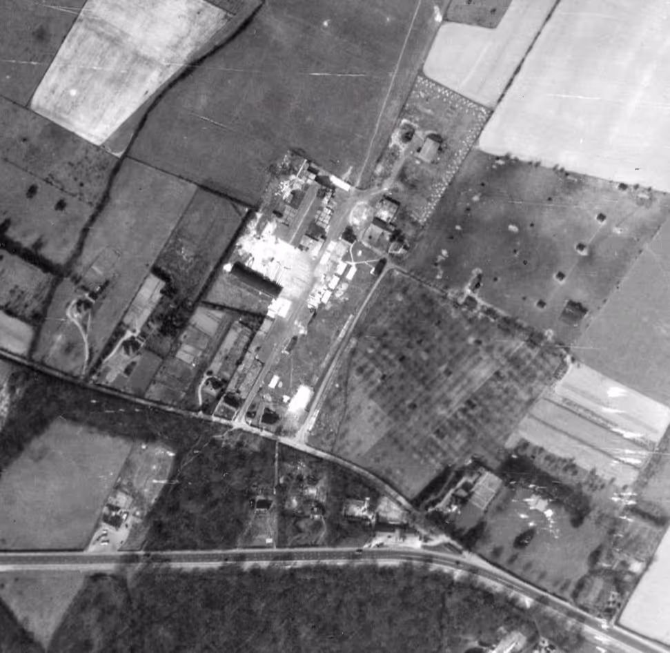 Black and white aerial view of rural farmland with fields, roads, and scattered buildings.