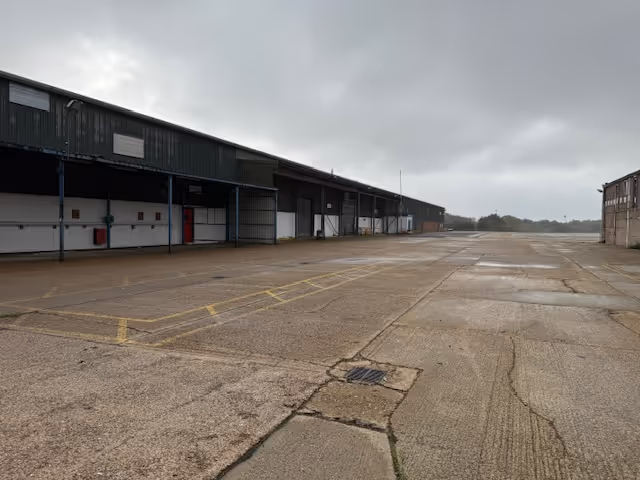 Empty industrial loading dock area with large warehouse buildings under a cloudy sky.