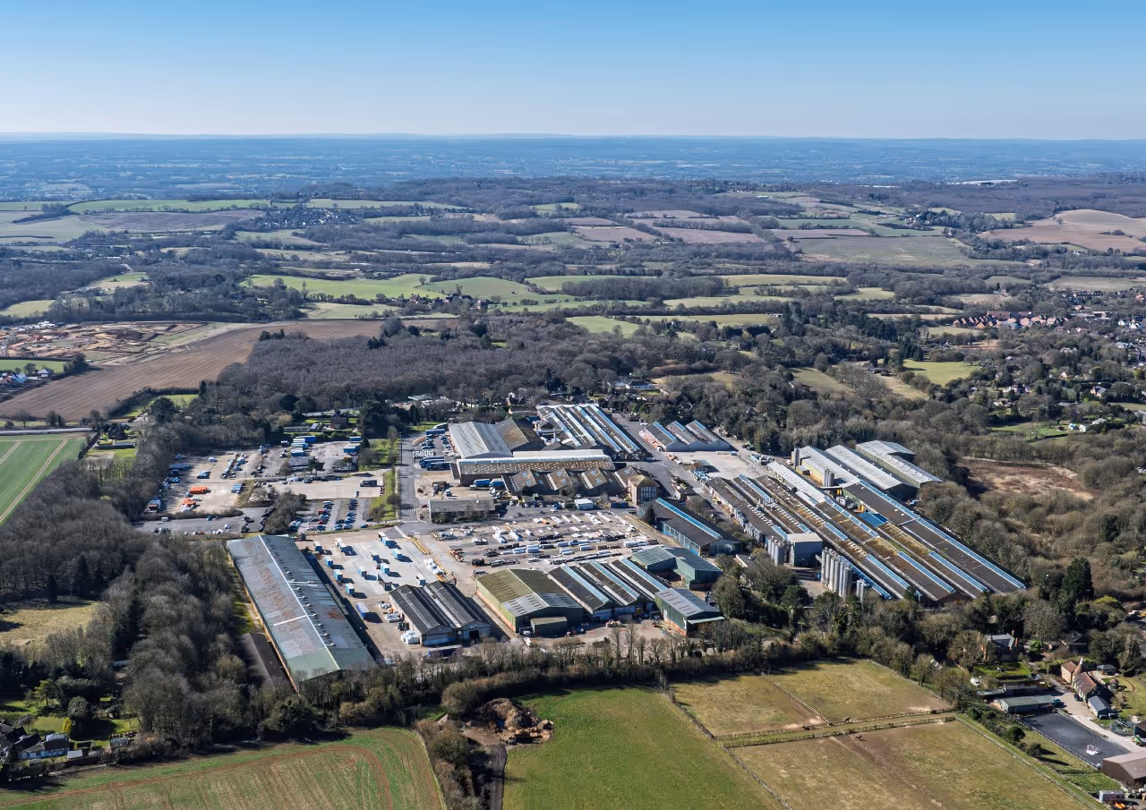 Aerial view of an industrial complex surrounded by fields and patches of woodland under a clear blue sky.
