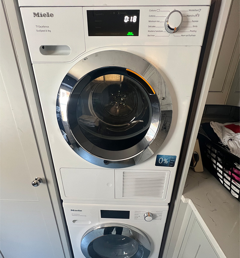 Stacked Miele front-loading washer and dryer unit inside a kitchen cabinet.