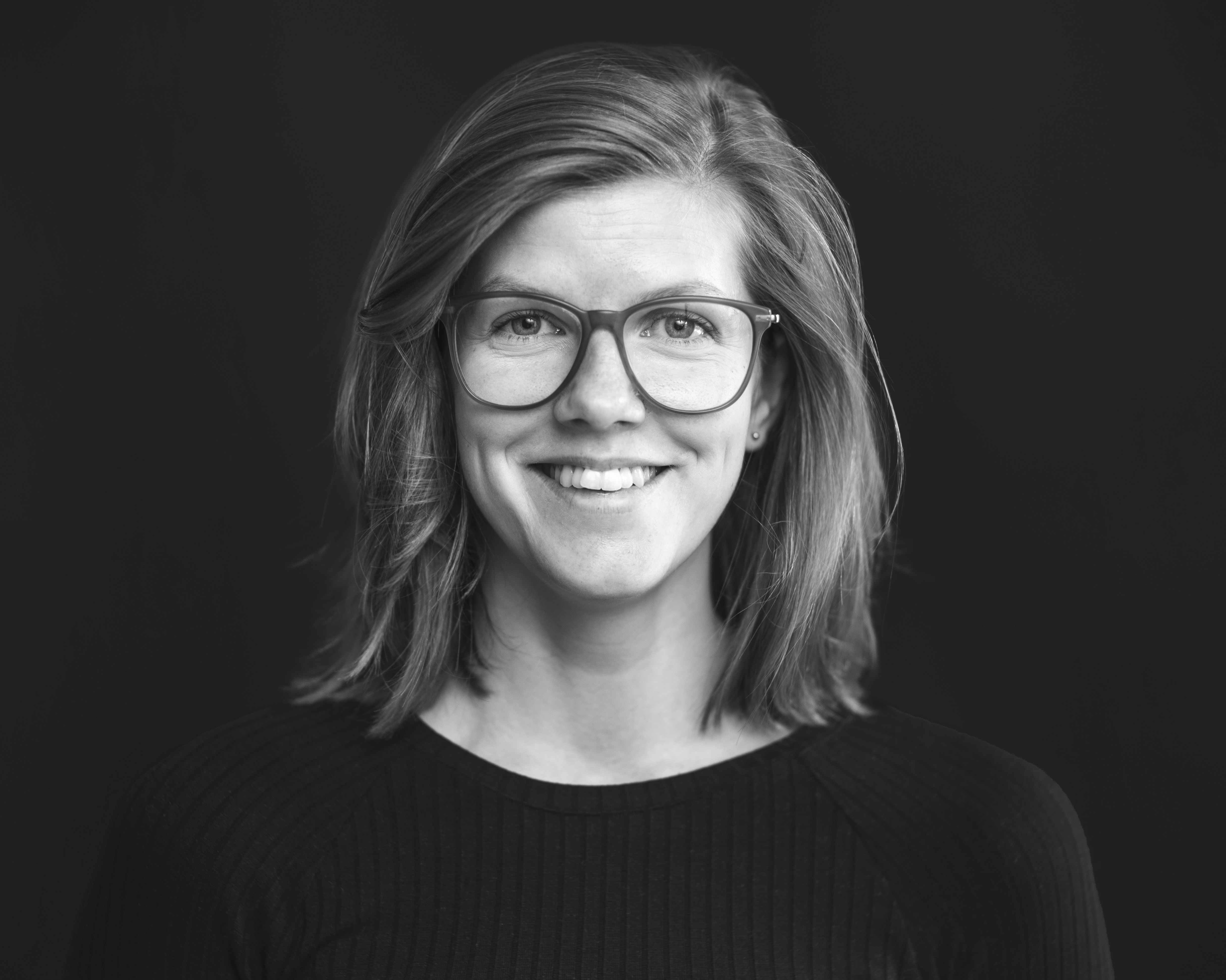 Ansattbilde i svart hvitt av en smilende kvinne med briller