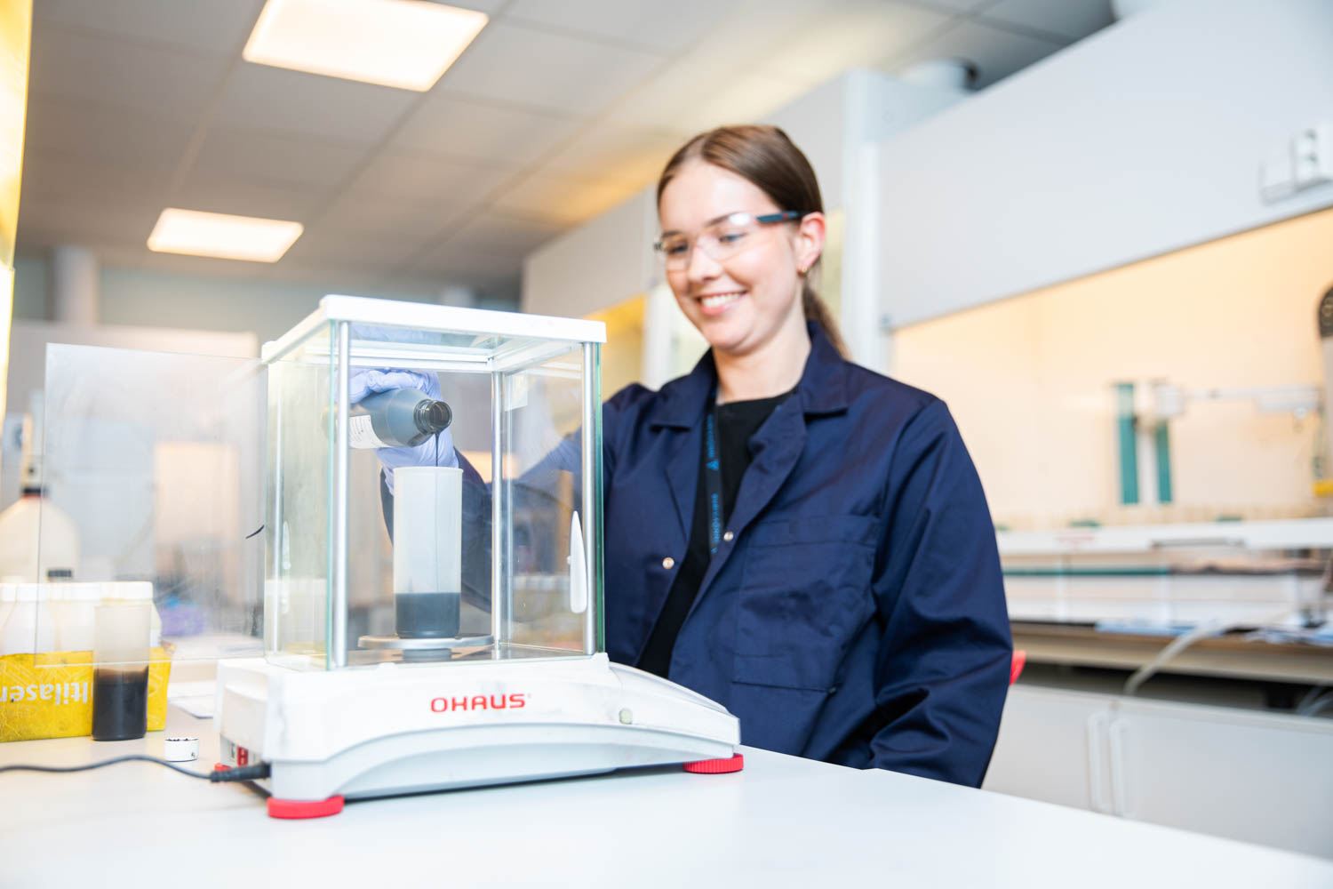 En ung kvinne står inne på en lab og jobber med en mørk væske