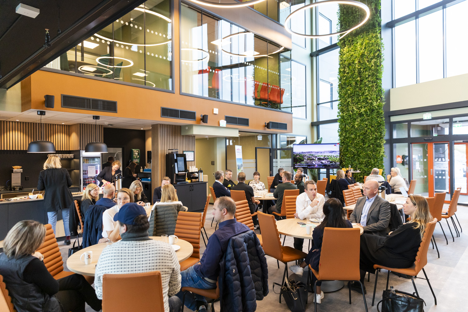Et oversiktsbilde av et fellesareal med folk som sitter rundt flere rundbord