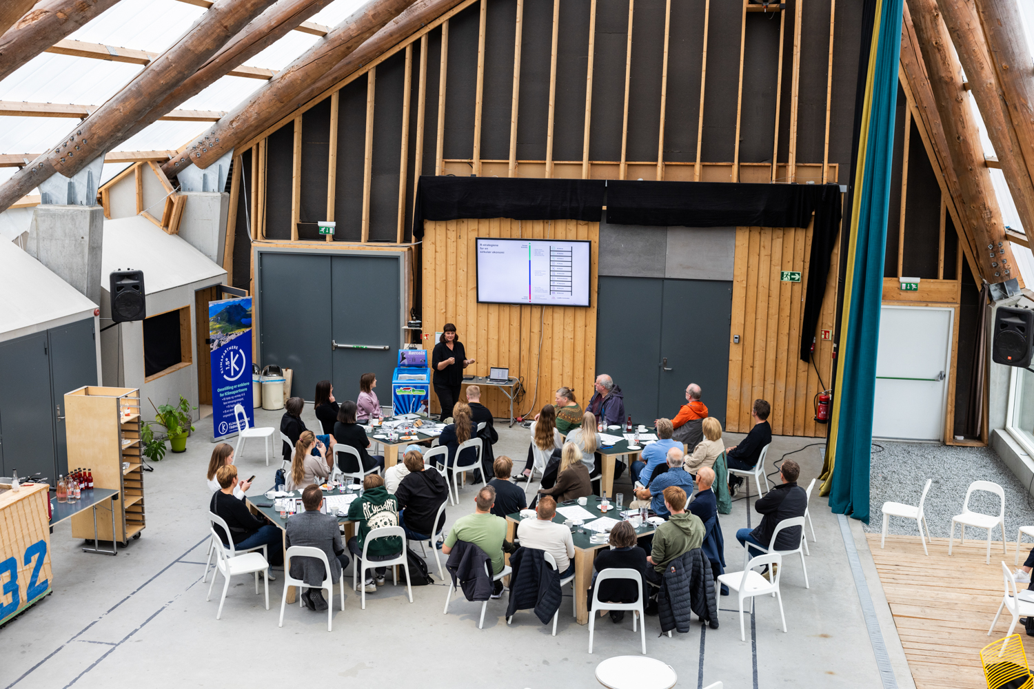 Et oversiktsbilde av et stort åpent rom med folk som følger med på en presentasjon