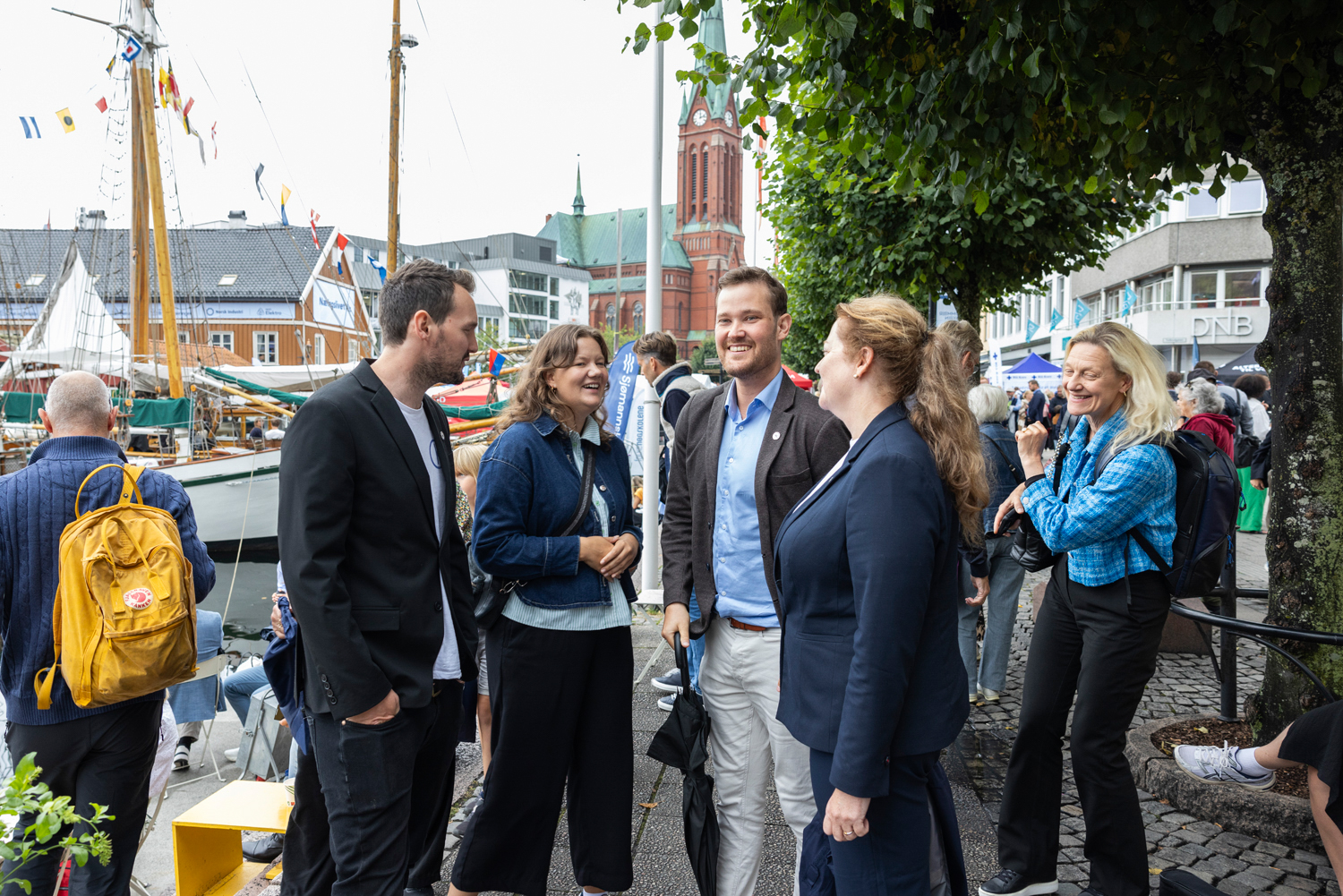 En liten gruppe pent kledde mennesker står ute ved en havn og prater sammen