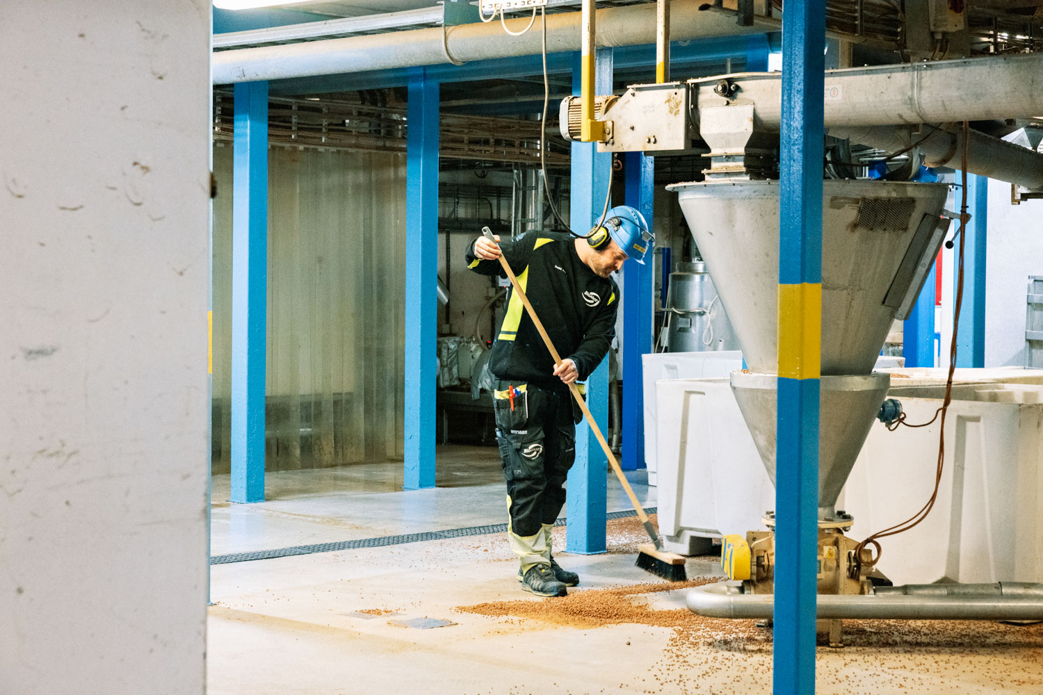 En mann med vernehjelm koster pellets på gulvet inne på en fabrikk