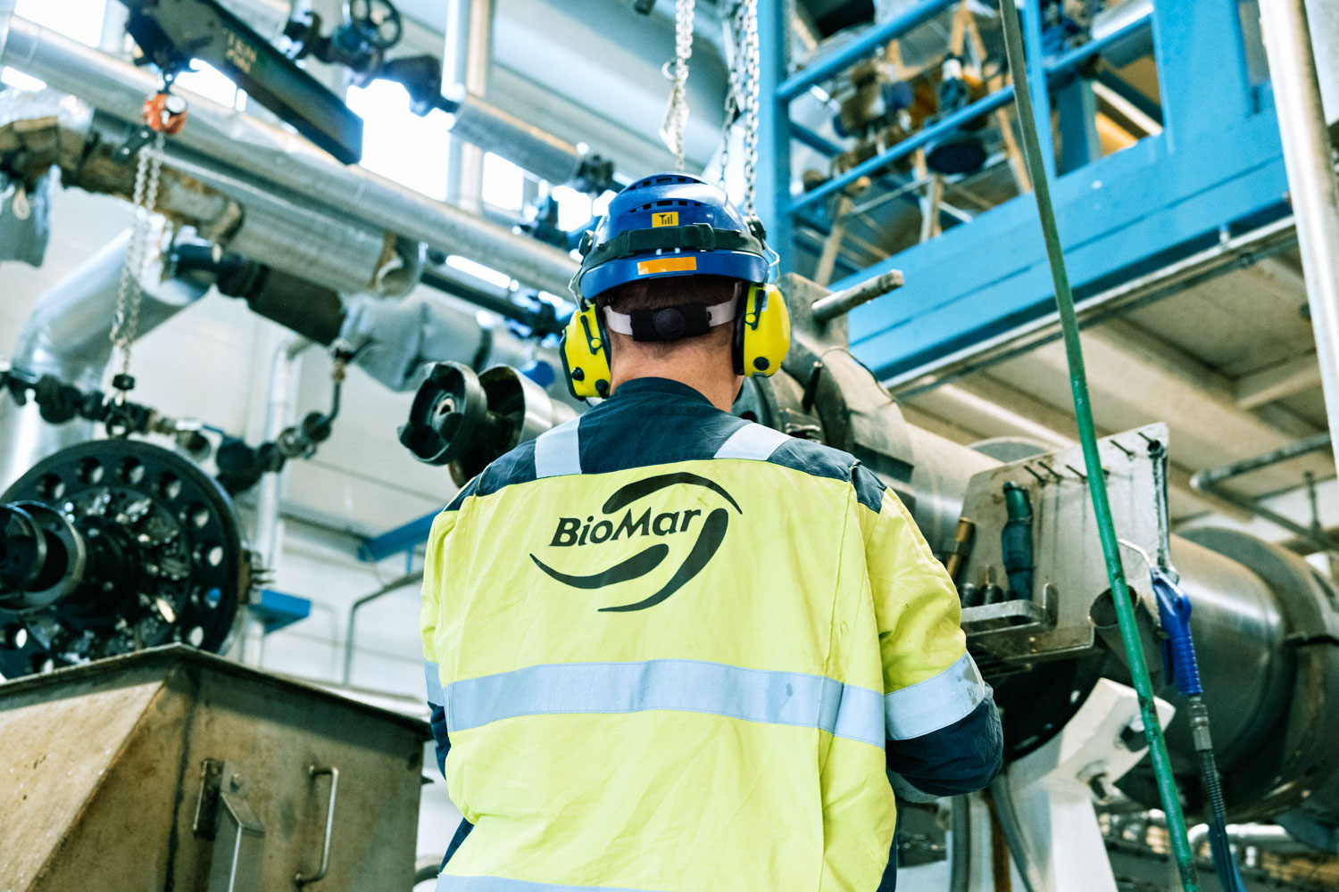Undervinklet foto av en mann iført synlighetsklær og verneutstyr som jobber inne på en fabrikk