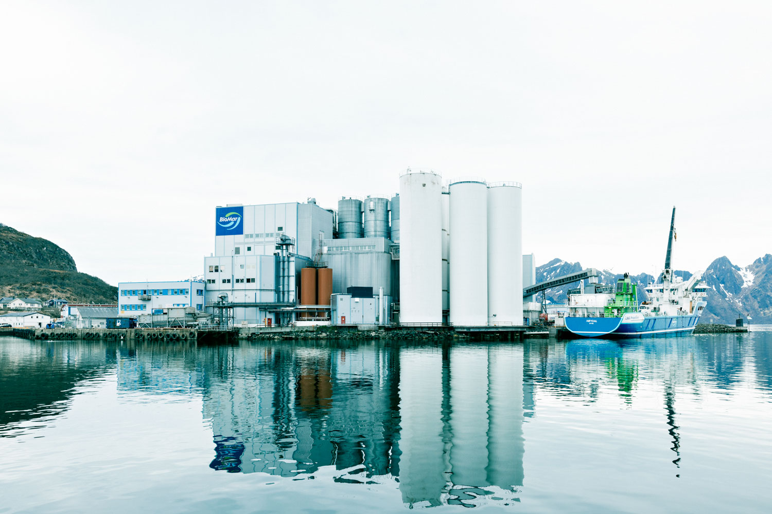 Fasaden av fabrikken til BioMar speiler seg i blikkstille hav