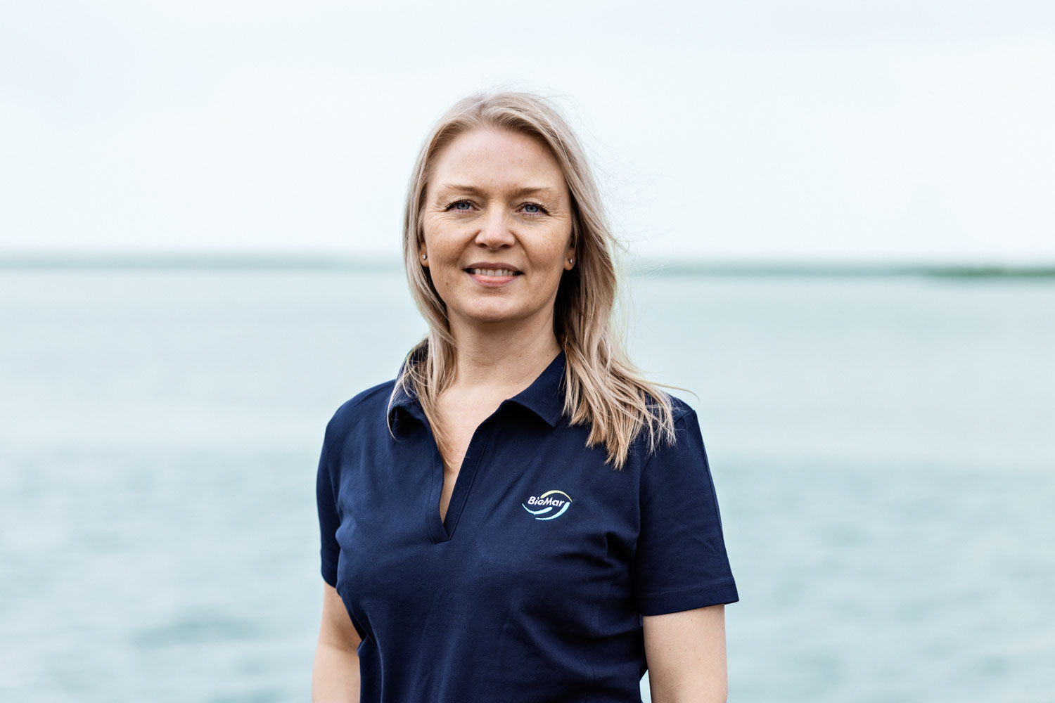 Portbilde av en kvinne som ser i kamera og smiler foran havet