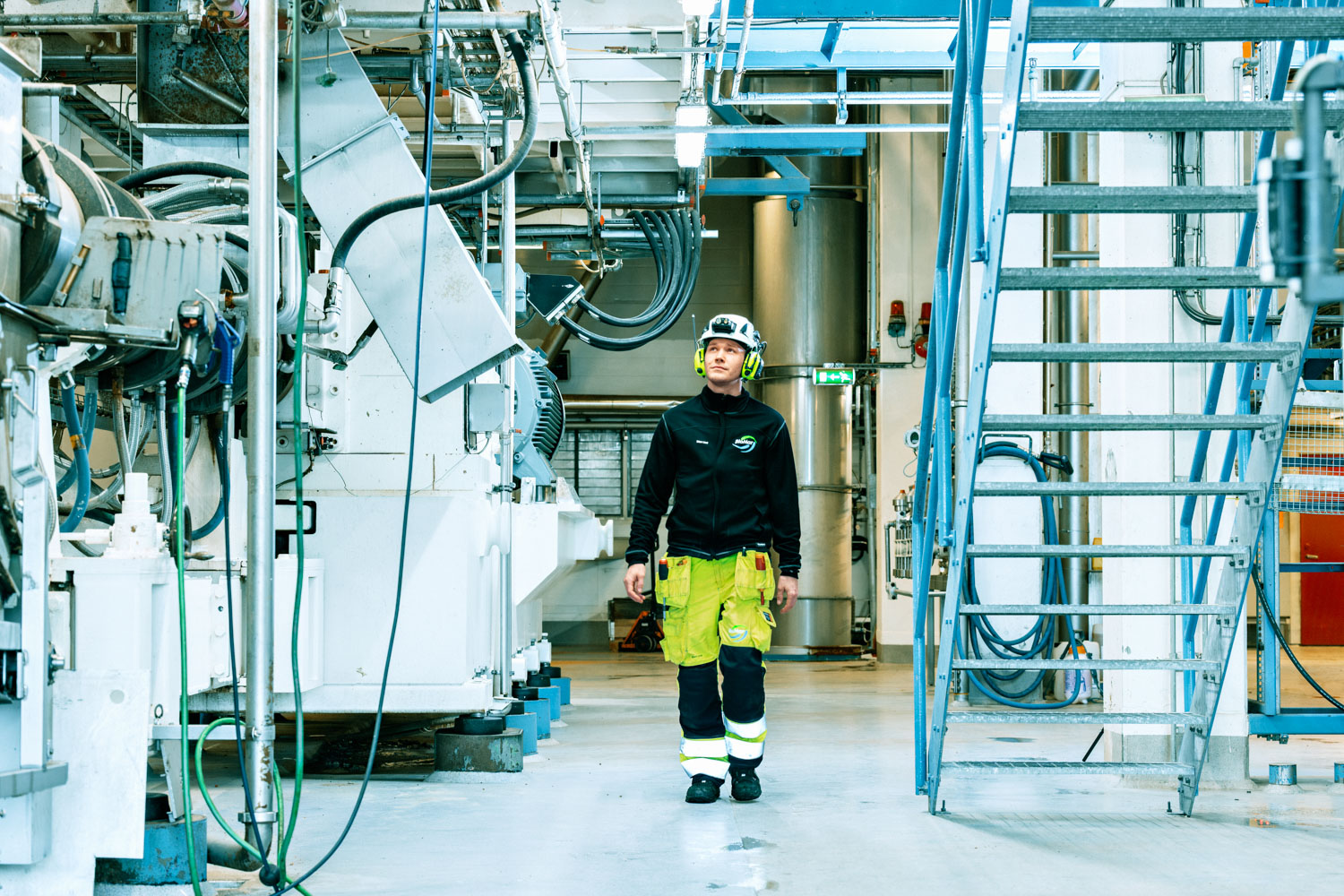 En mann iført synlighetsklær og verneutstyr går inne på en fabrikk