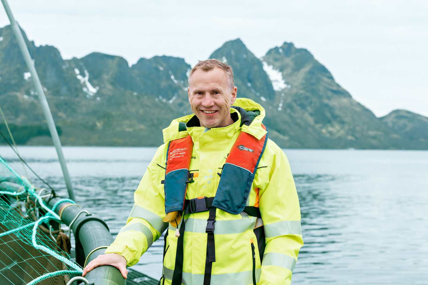 En mann iført synlighetsklær står på en merde og smiler til kamera