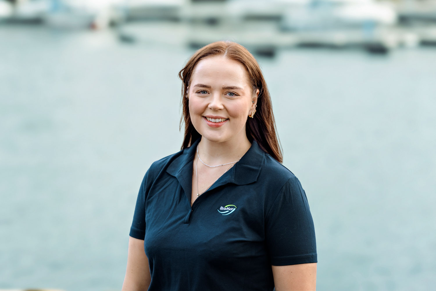 En ung kvinne står foran havet med en båtbrygge i bakgrunn
