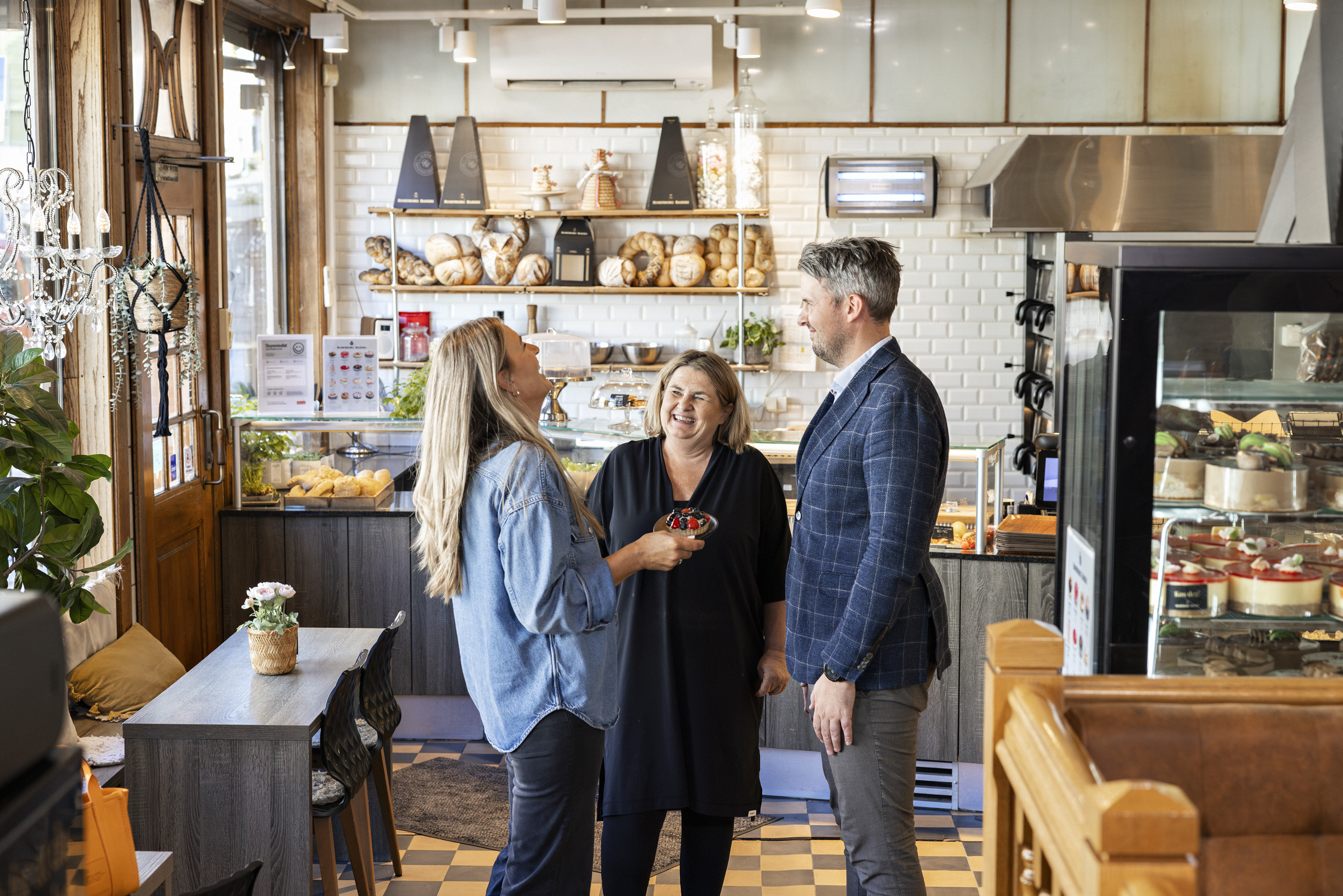 Tre dresskledde personer står og hygger seg inne på en kafé