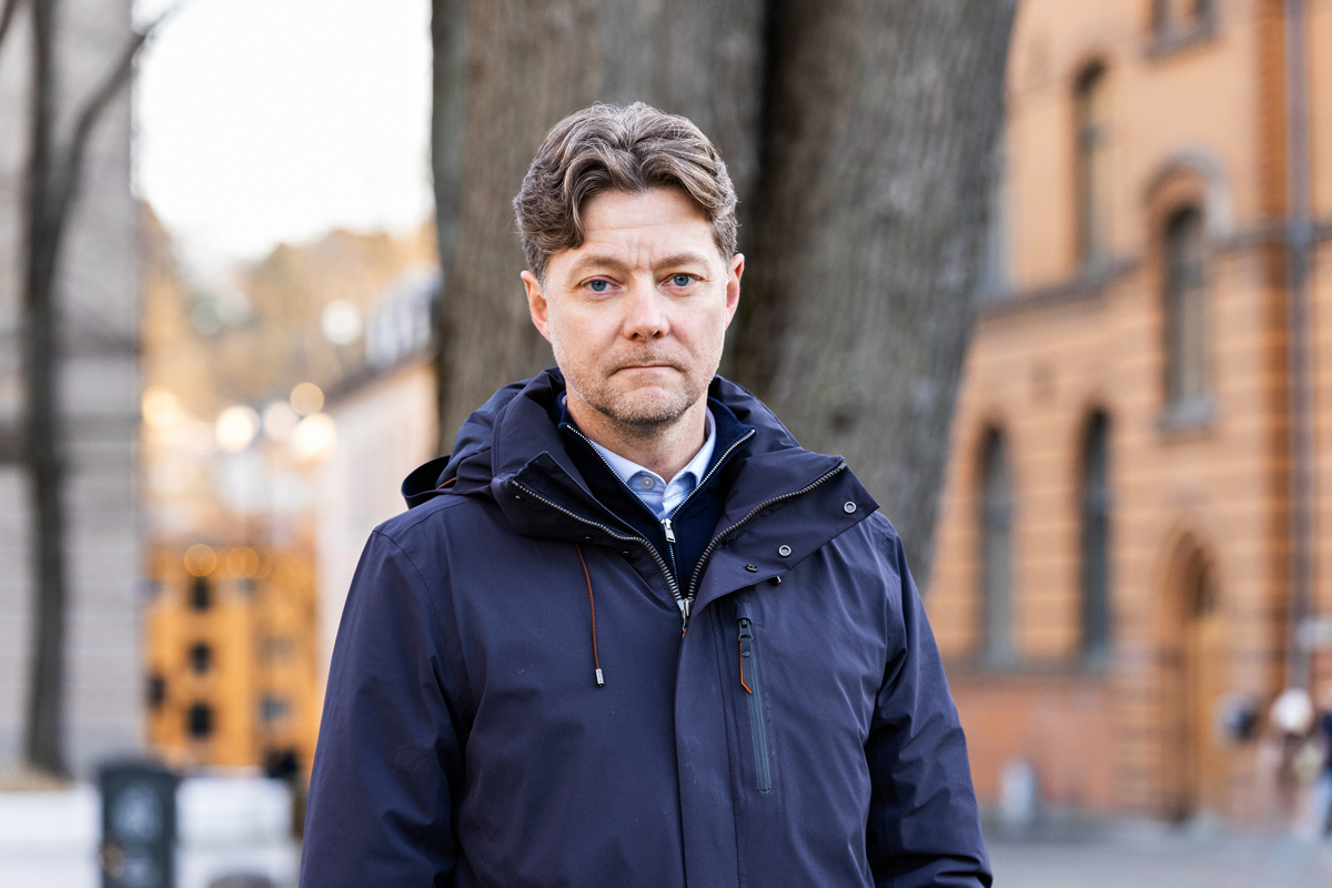 En mann står ute på en gate iført jakke mens han ser i kamera