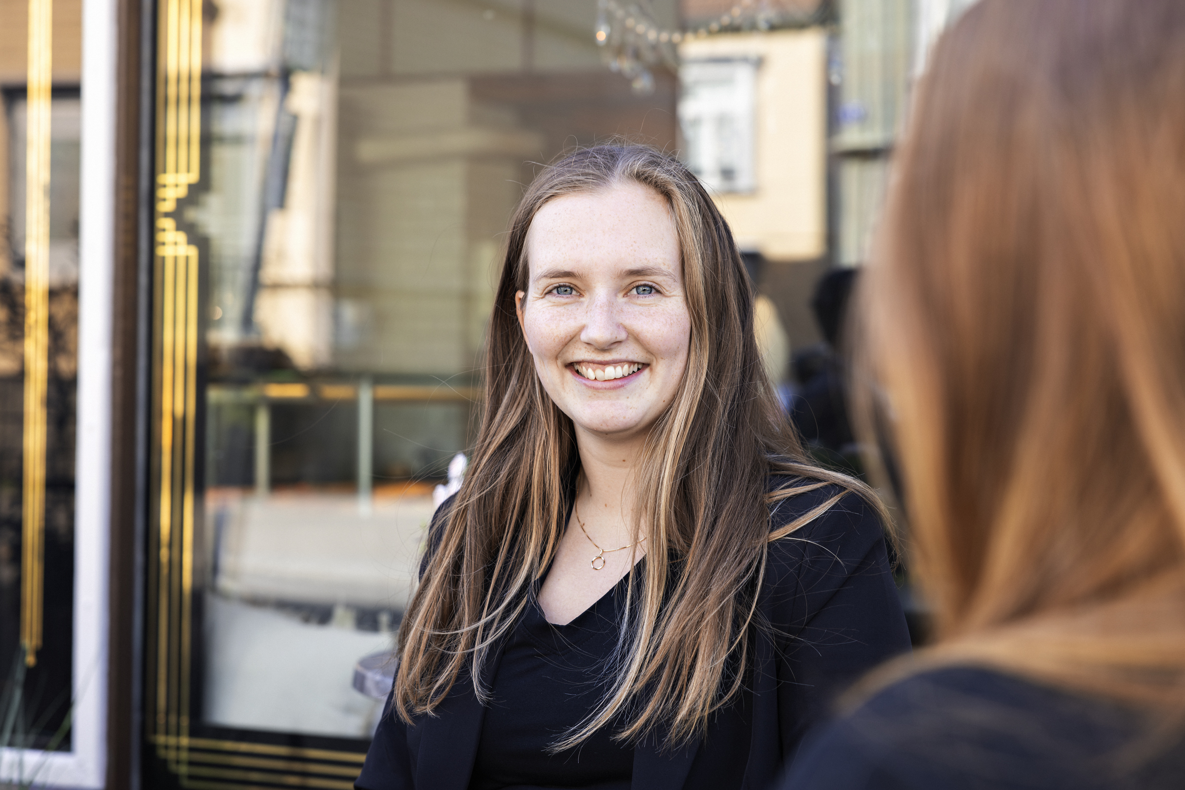En ung kvinne står utenfor en kafé og smiler til kamera