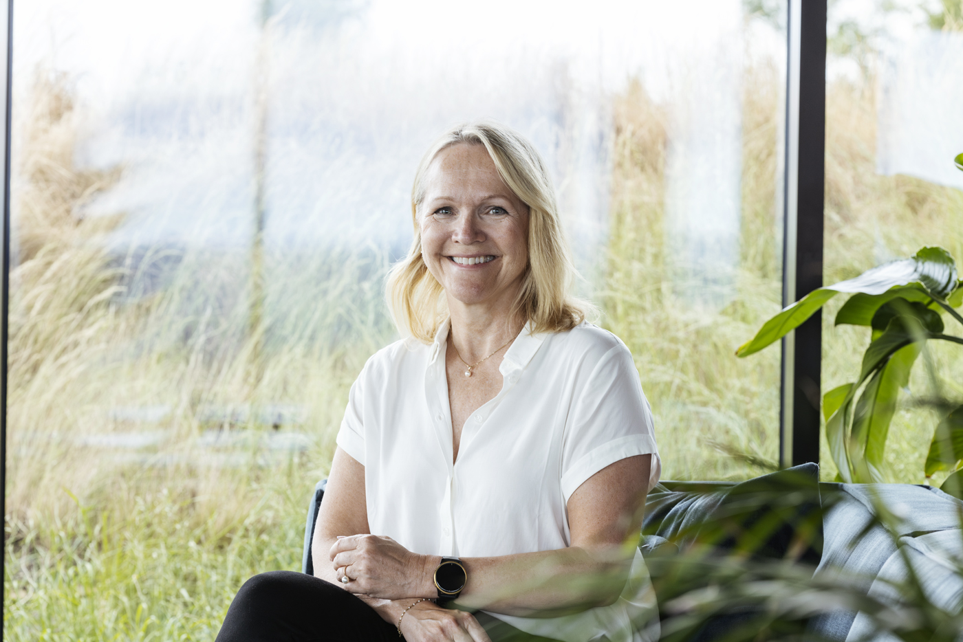 En lyskledd kvinne sitter ved en glassvegg og smiler til kamera