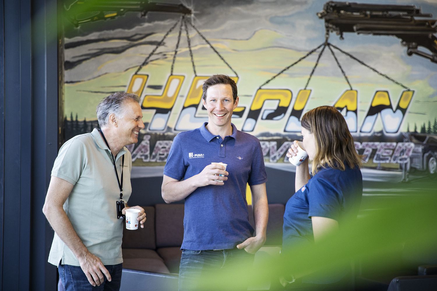 Tre kollegaer står sammen og drikker kaffe i et moderne kontorlandskap