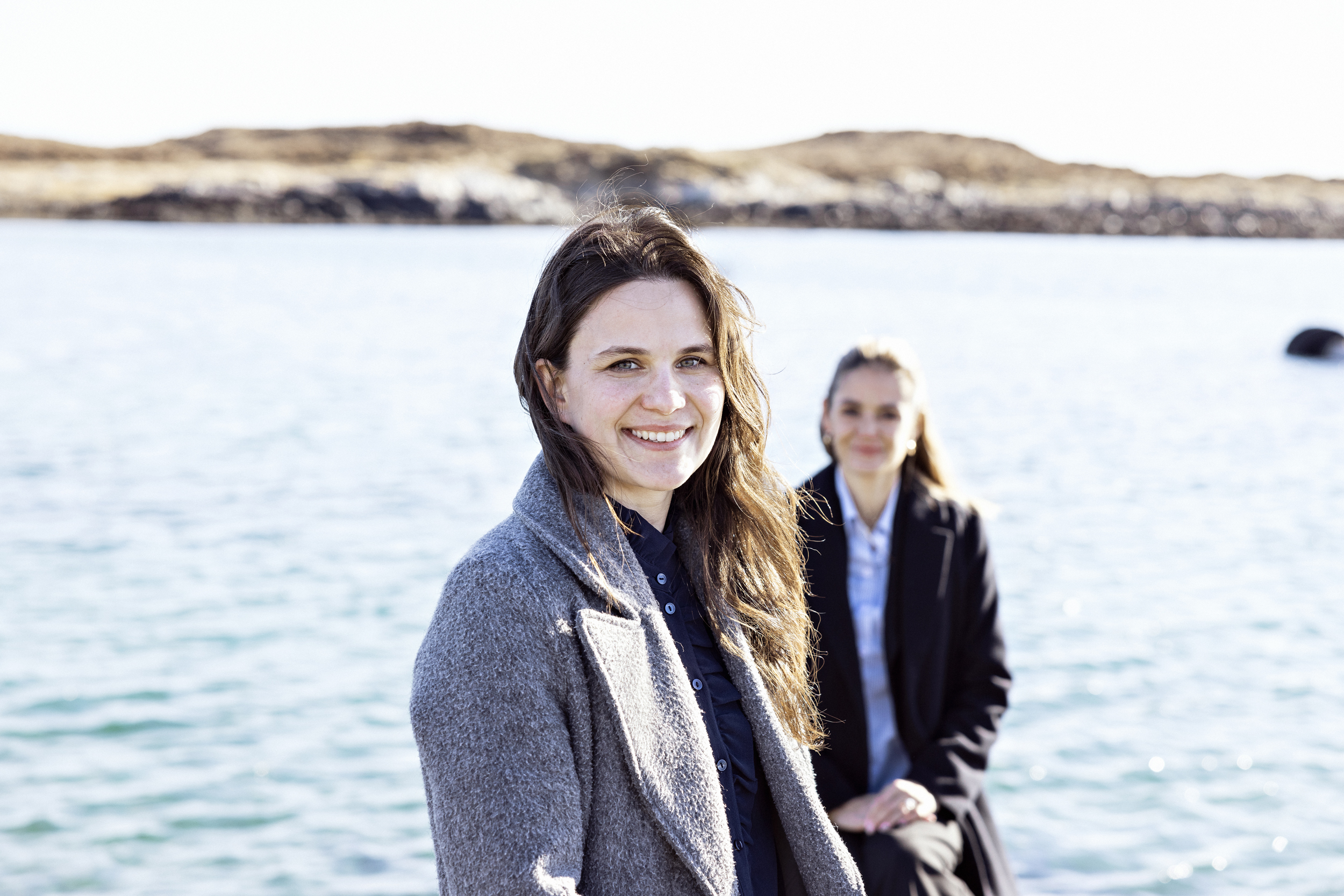 To kvinner står ute foran havet og ser i kamera