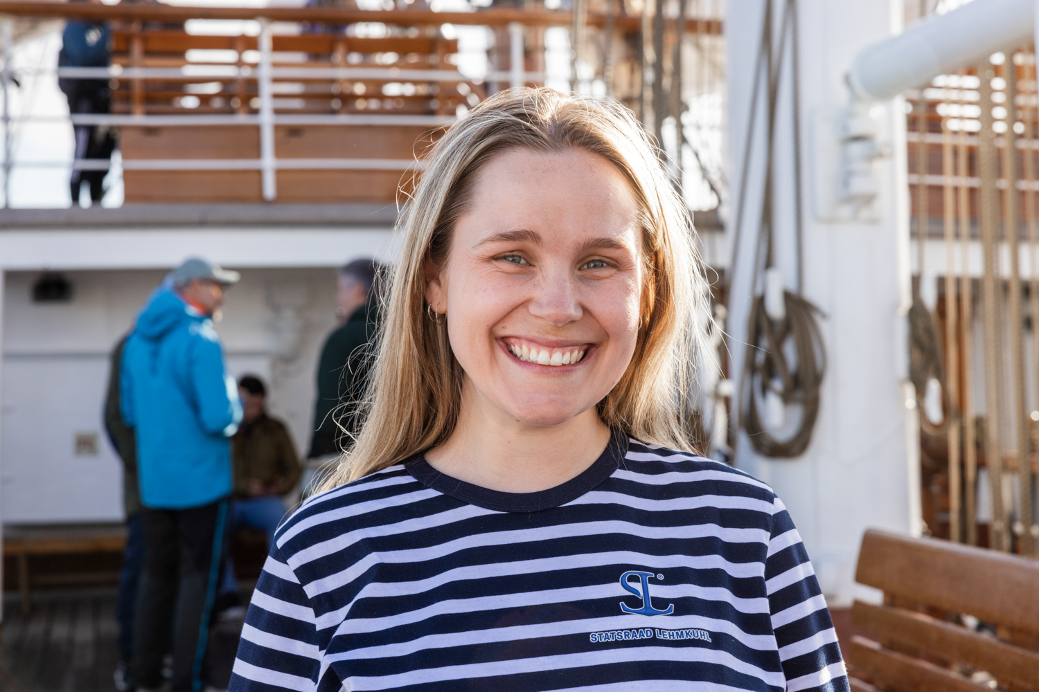 En ung kvinne iført stripete t-skjorte smiler til kamera mens hun står på båtdekk