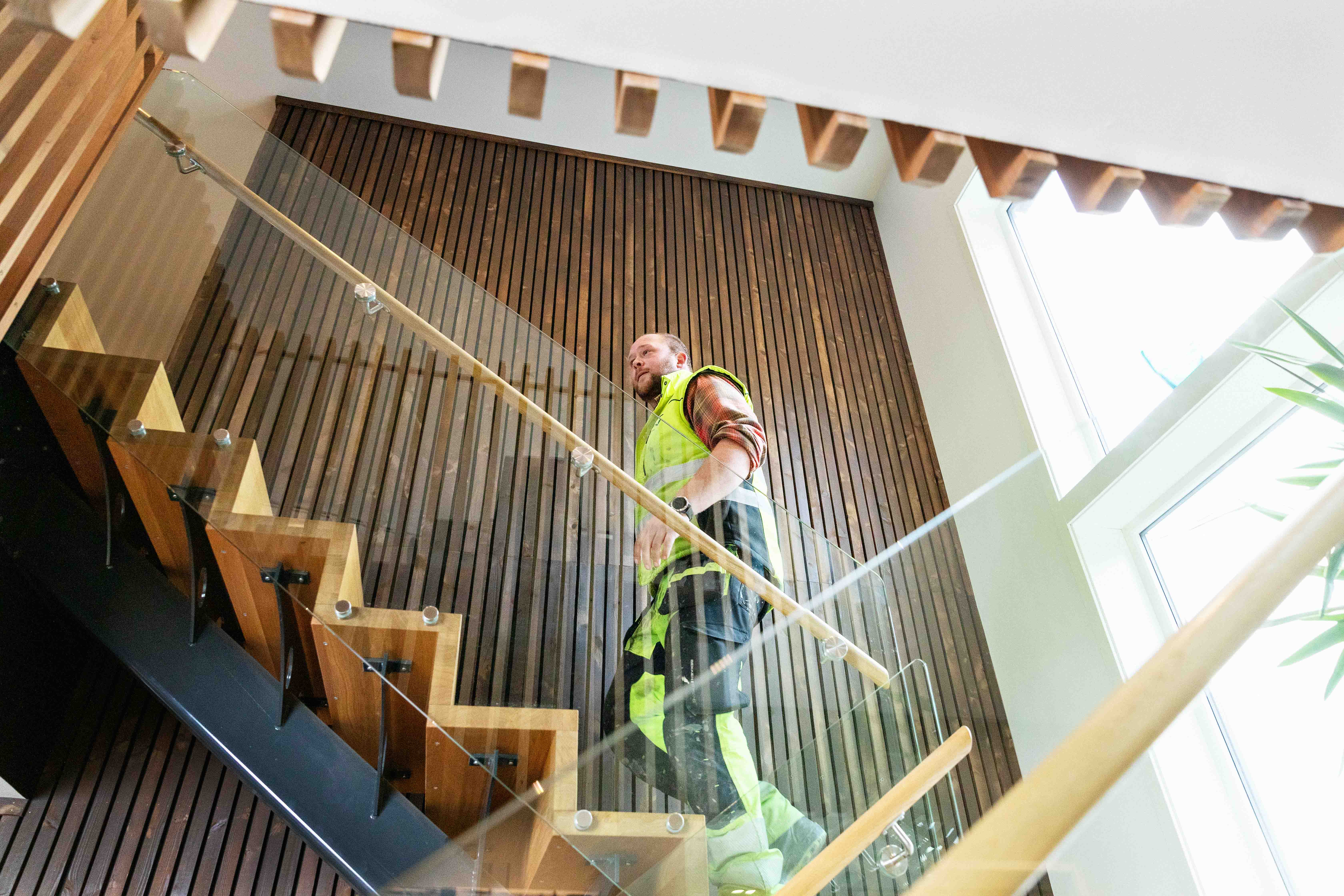 En mann i synlighetsklær går opp en trapp i moderne kontorlokale.