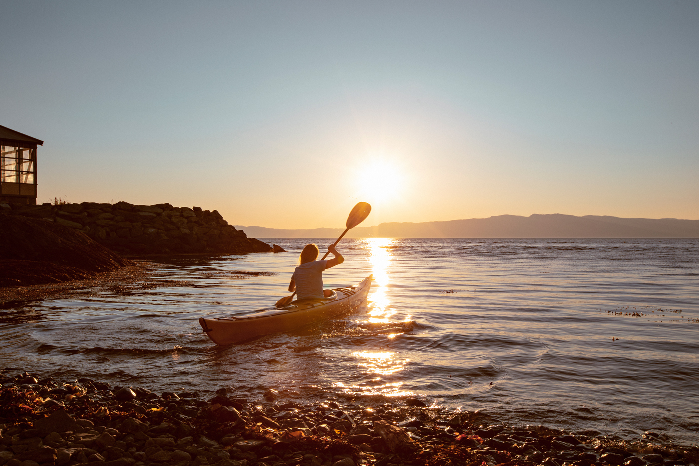 En kvinne som padler i en kajakk i havet mens solen er på vei ned