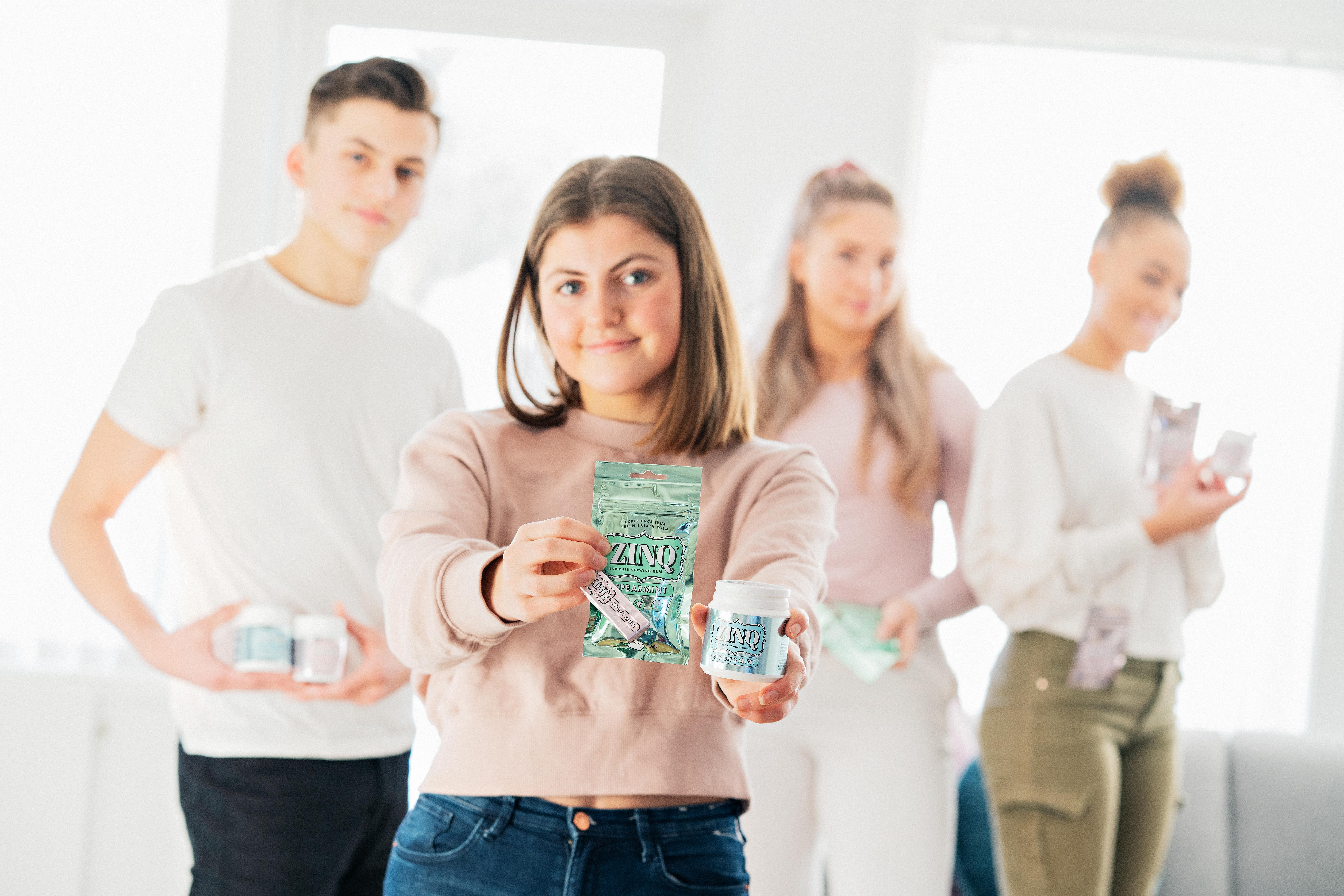 Unge mennesker holder opp produkter for Zinq, alle ser i kamera