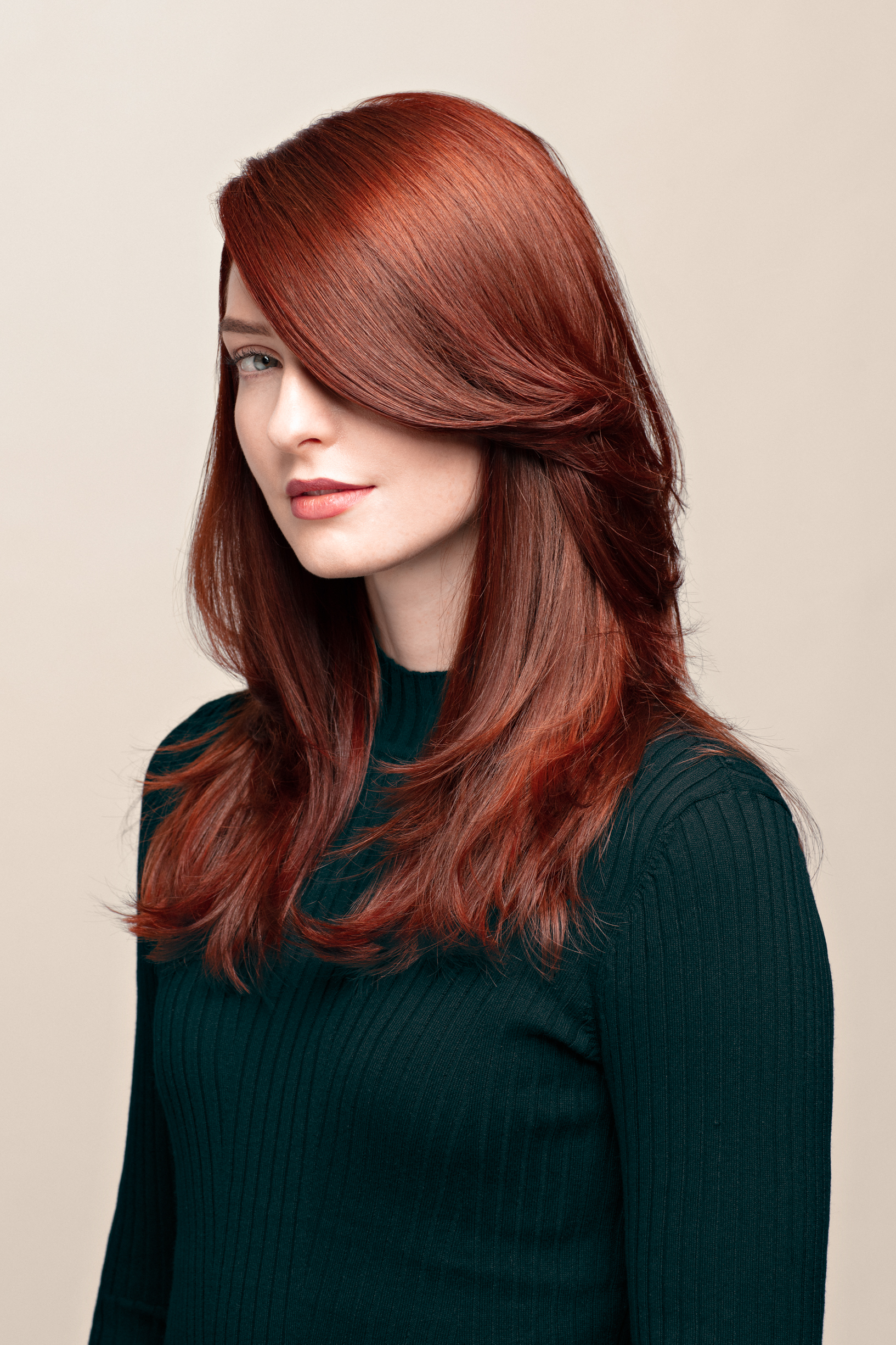 En ung kvinne med rødt langt hår poserer i et beige-farget studio