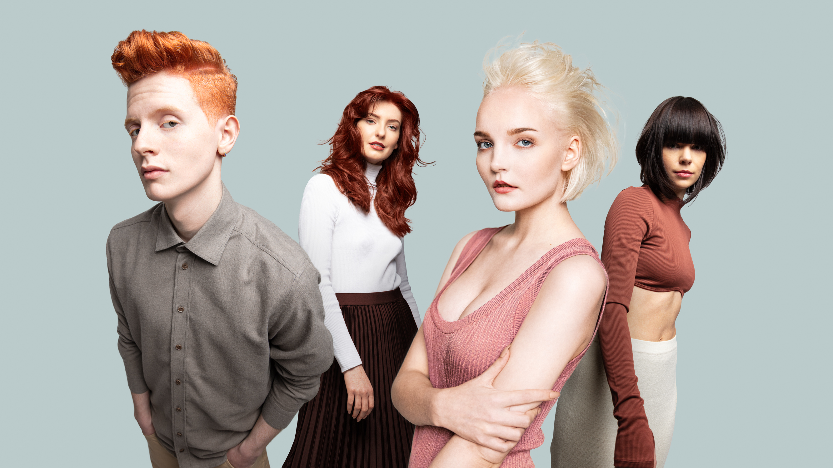 Fire unge mennesker ser i kamera mens de poserer i et studio med dus blå bakgrunn