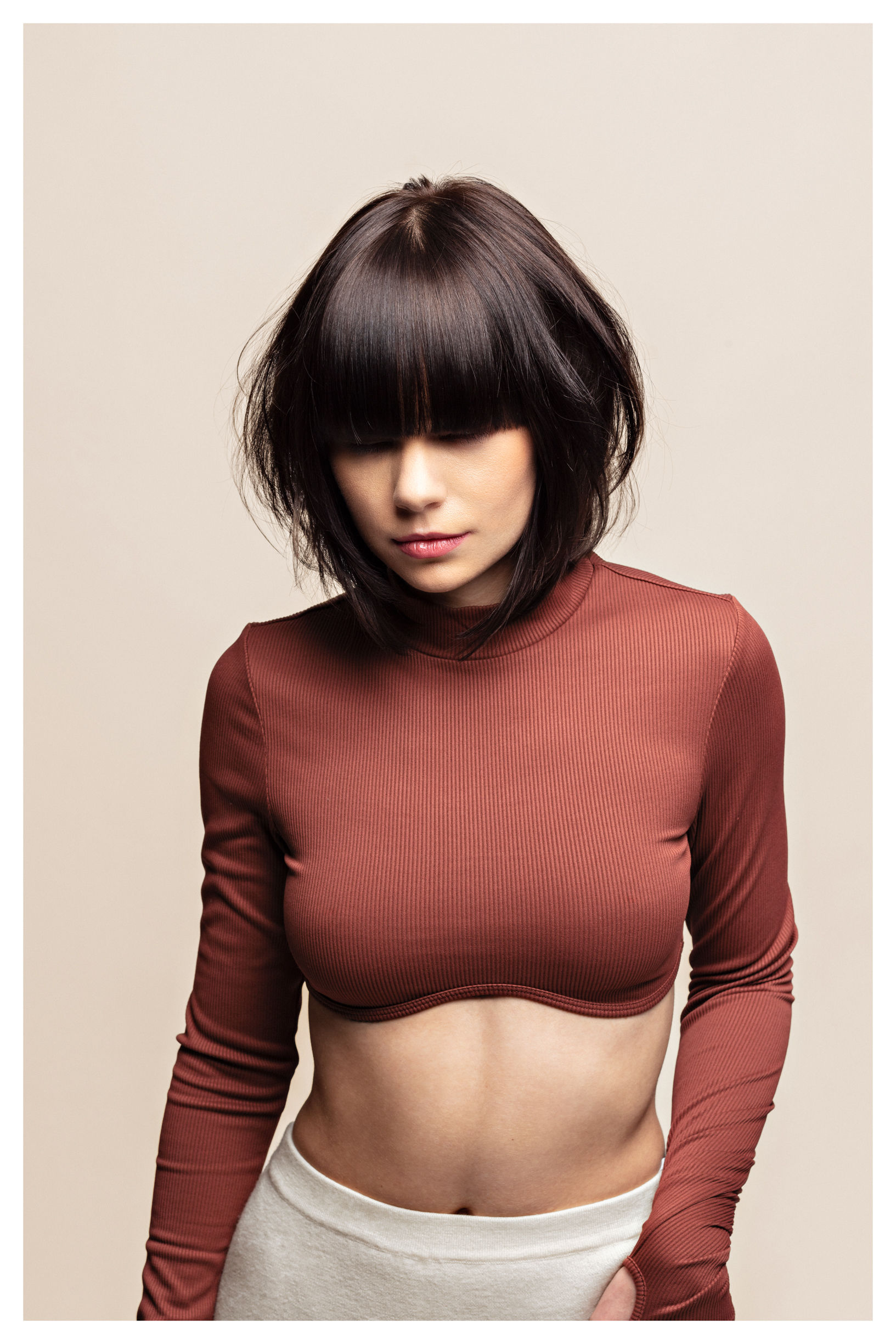 En ung kvinne med mørkt hår poserer i et studio med beige bakgrunn