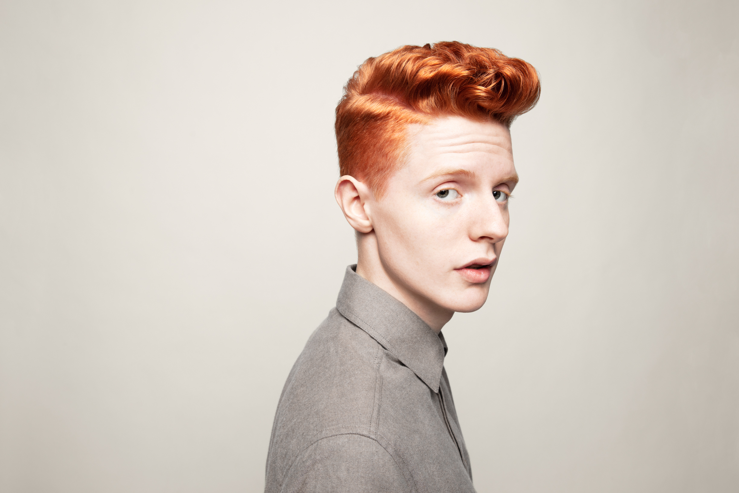 En ung mann med rødt kort hår ser inn i kamera i et studio med ensfarget bakgrun
