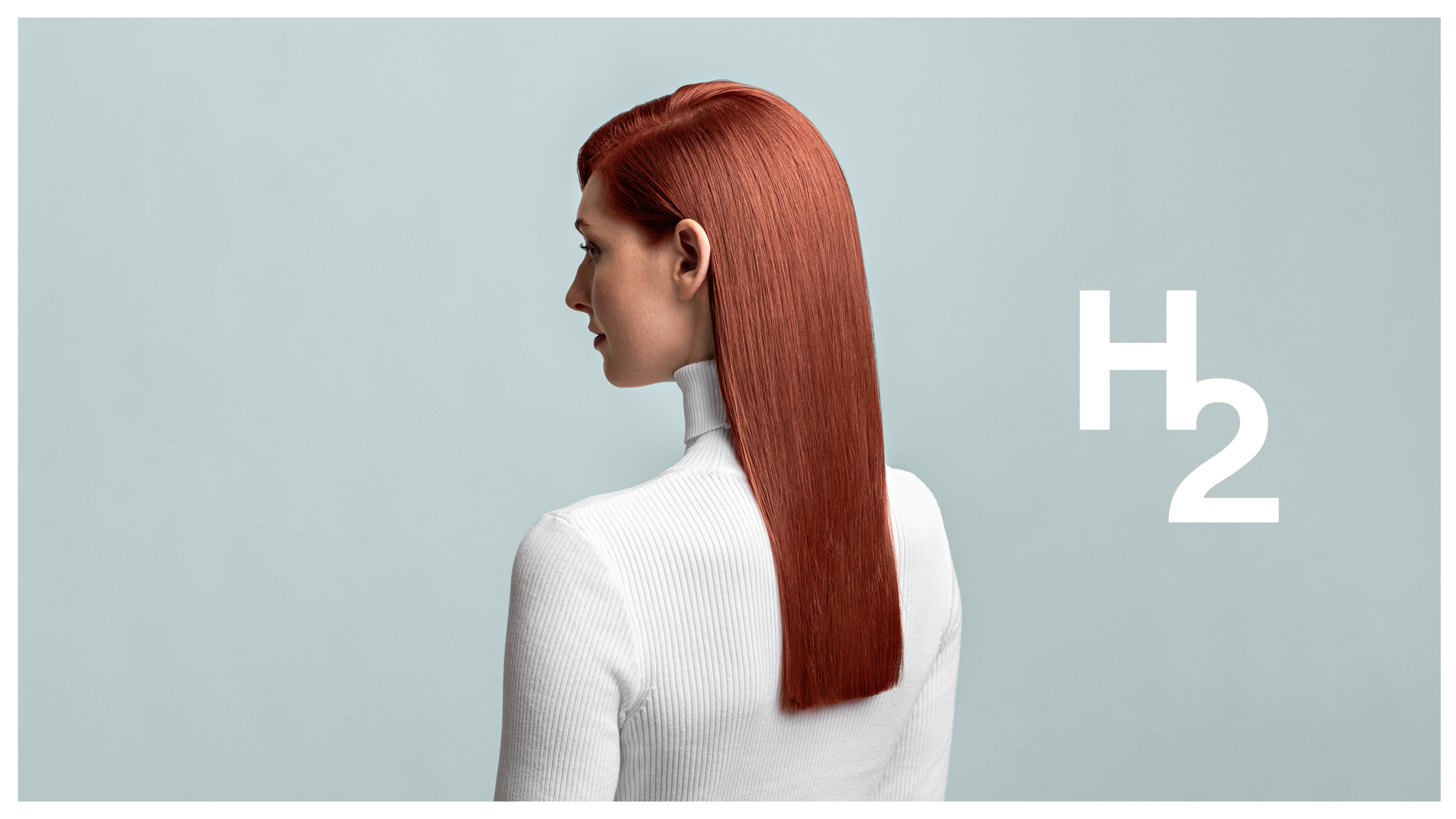 En ung kvinne med rødt langt hår poserer med ryggen mot kamera med en ensfarget dus blå bakgrunn