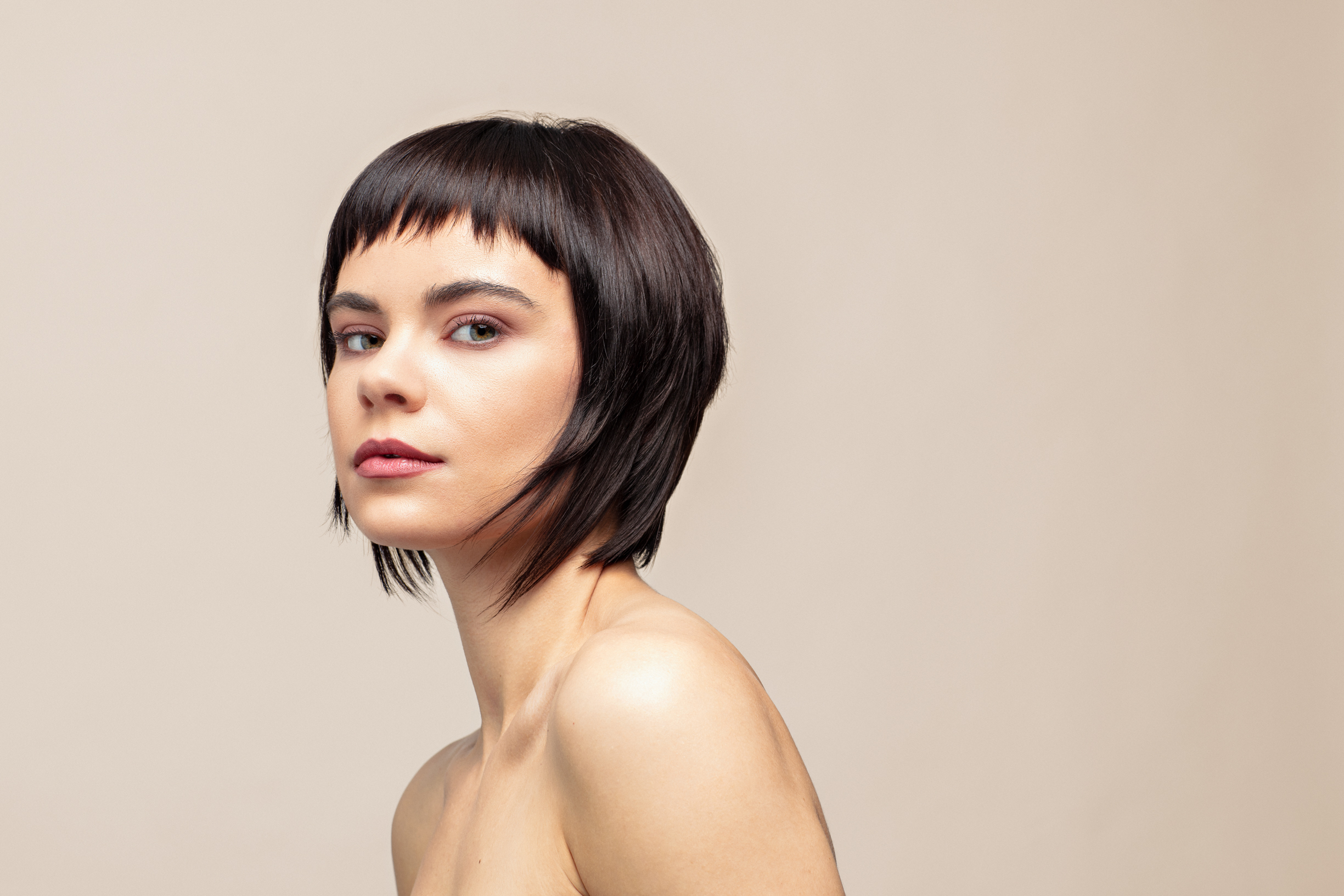 En ung kvinne med mørkt hår poserer i et studio med beige bakgrunn