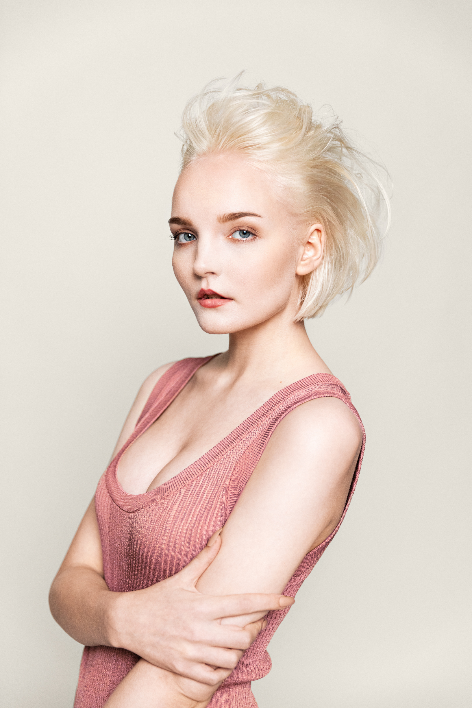 En ung kvinne med lyst hår poserer og ser i kamera med beige farget bakgrunn