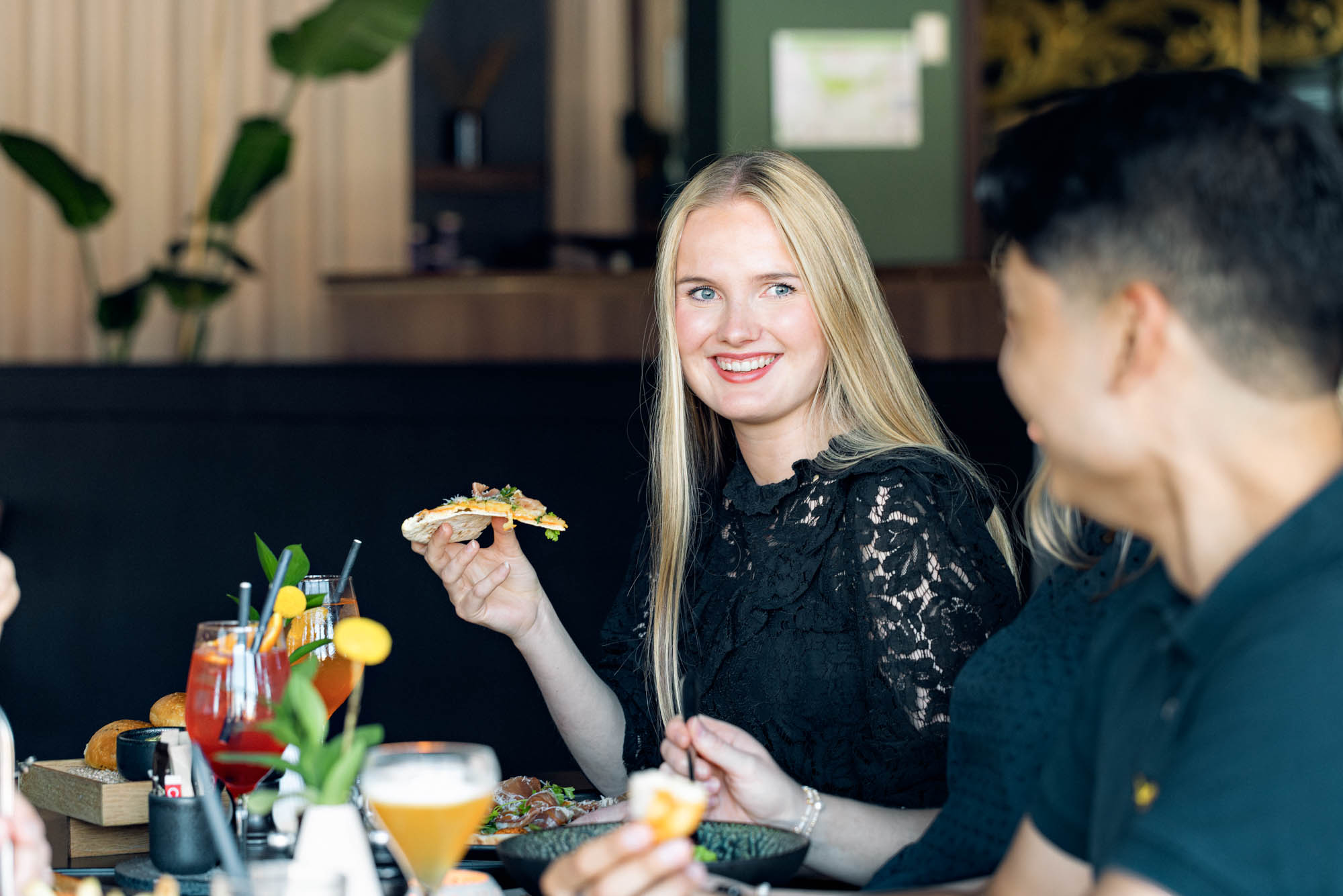 Ung kvinne holder opp et pizzastykke mens hun sitter med venner i fin hotelrestaurant
