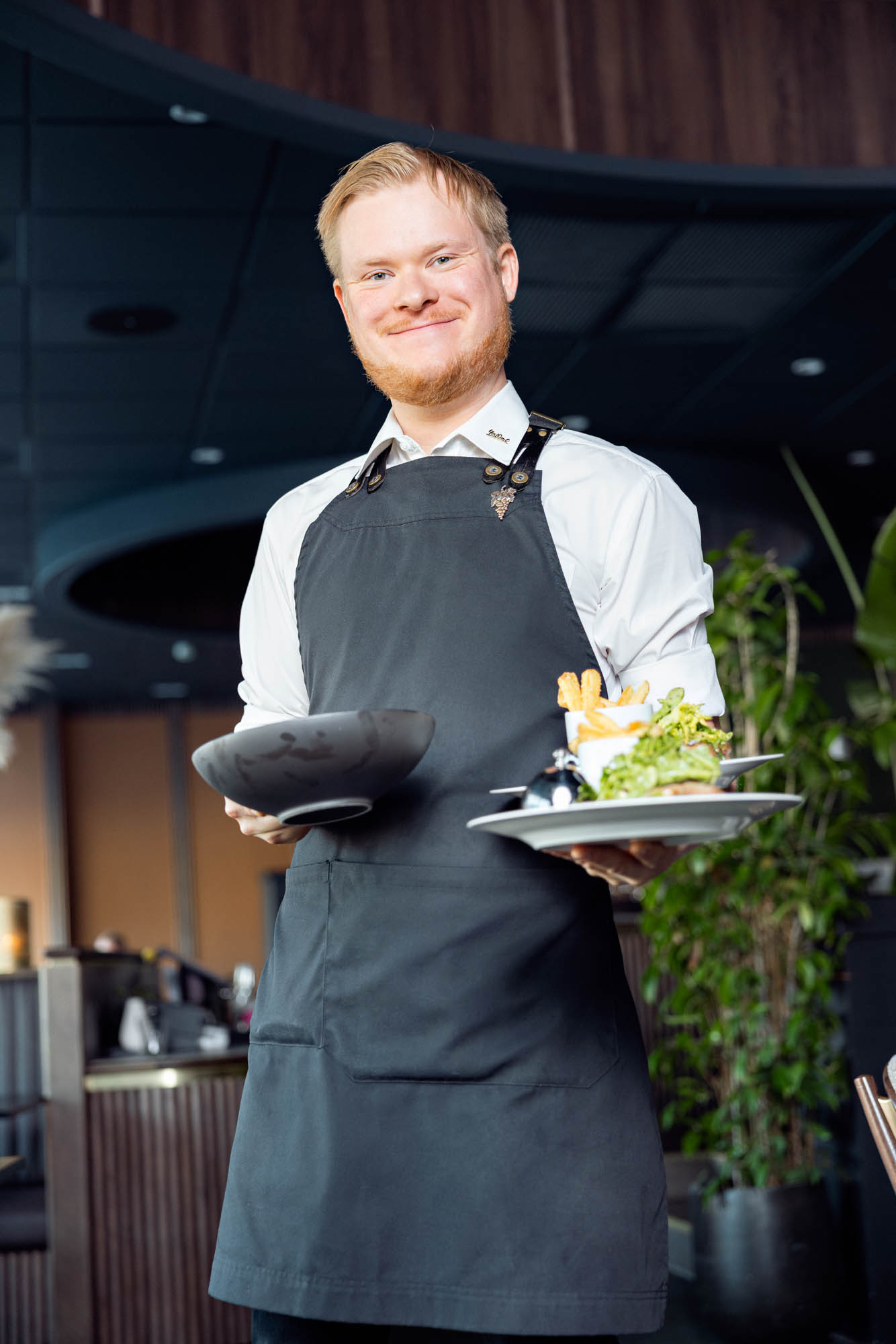 En servitør holder opp to tallerkener med mat i en fin hotelrestaurant
