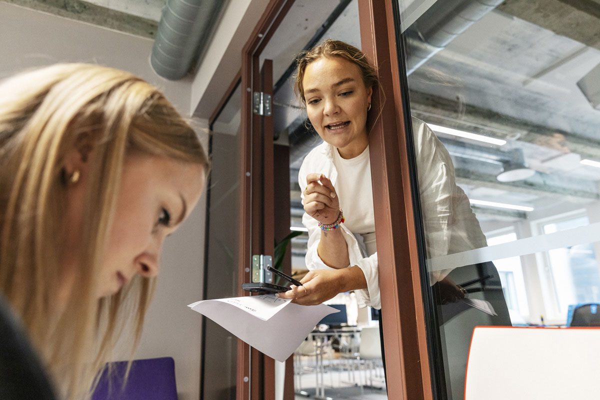 Kollegaer som konverserer i møterom i moderne kontorlandskap