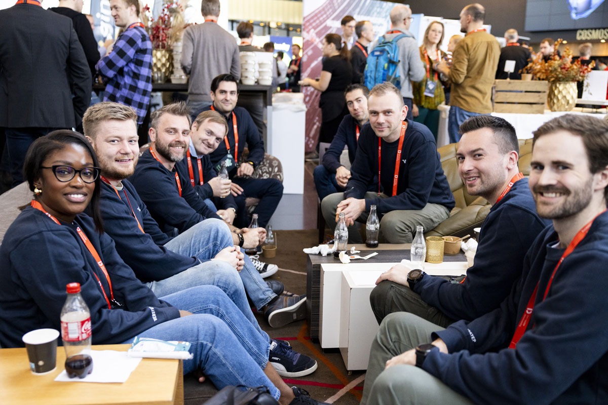 Flere mennesker ser mot kamera og smiler med en matkø i bakgrunnen