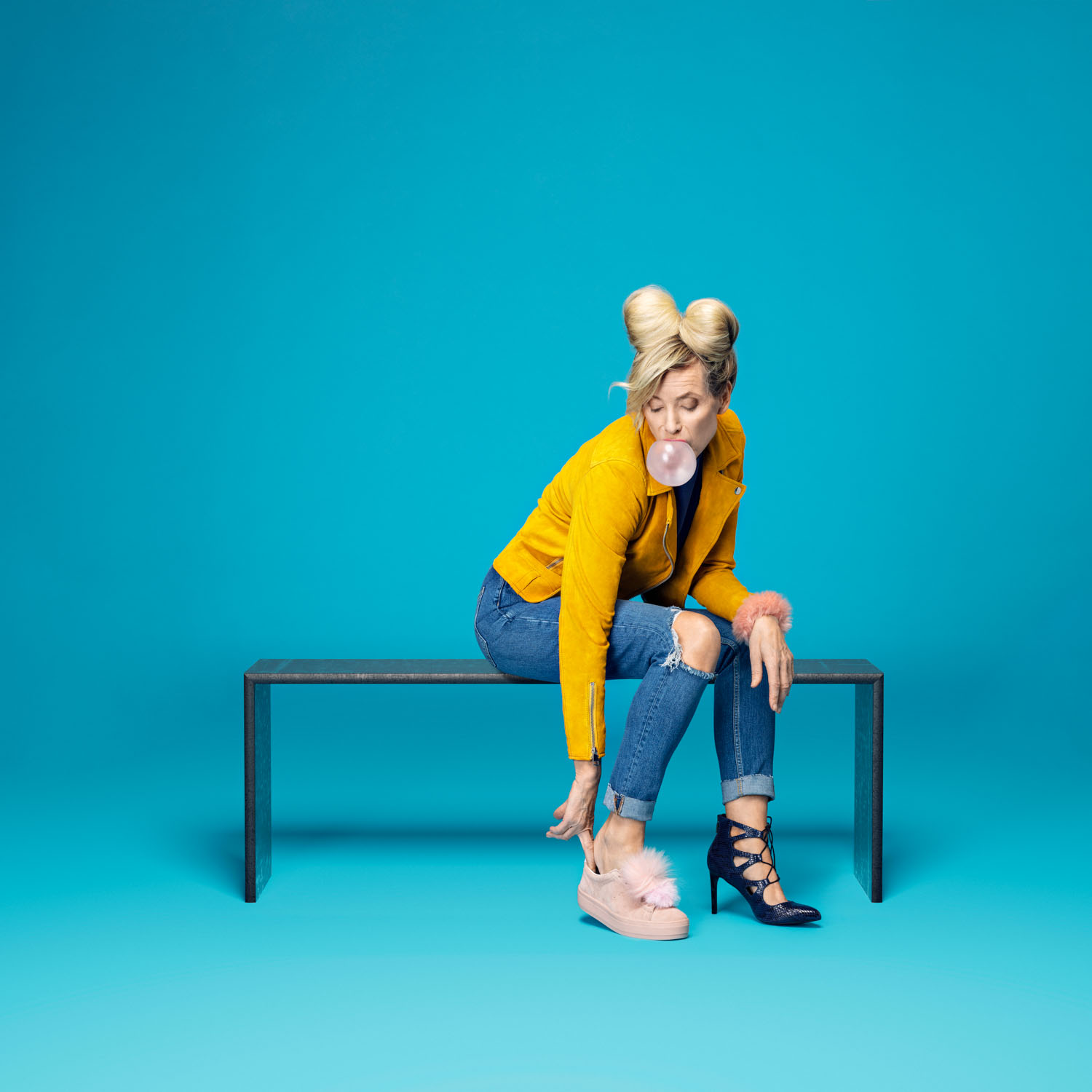 En kvinne iført gul jakke sitter på en benk foran en blåfarget bakgrunn i et fotostudio