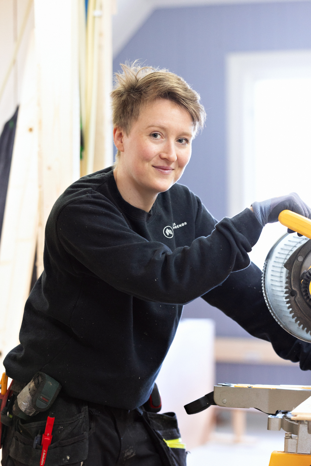 En kvinnelig ansatt fra Faanes Entreprenør smiler til kamera mens hun kapper treplanker