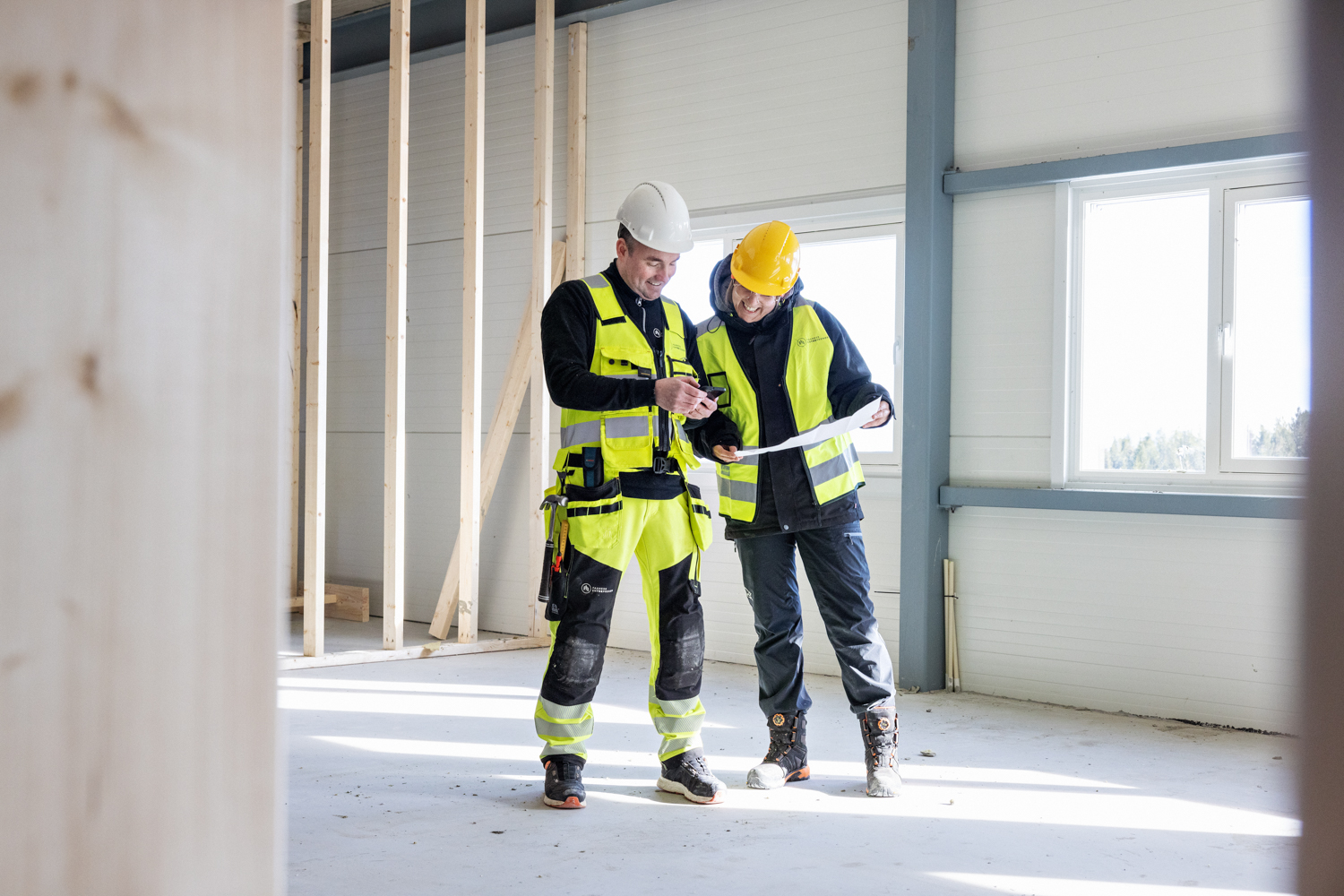 To byggningsarbeidere ser på plantegninger i et hus under konstruksjon