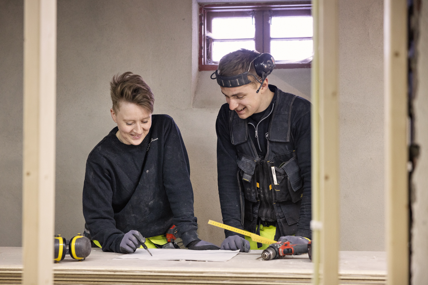 To tømrere står og ser på plantegninger i et hus under konstruksjon
