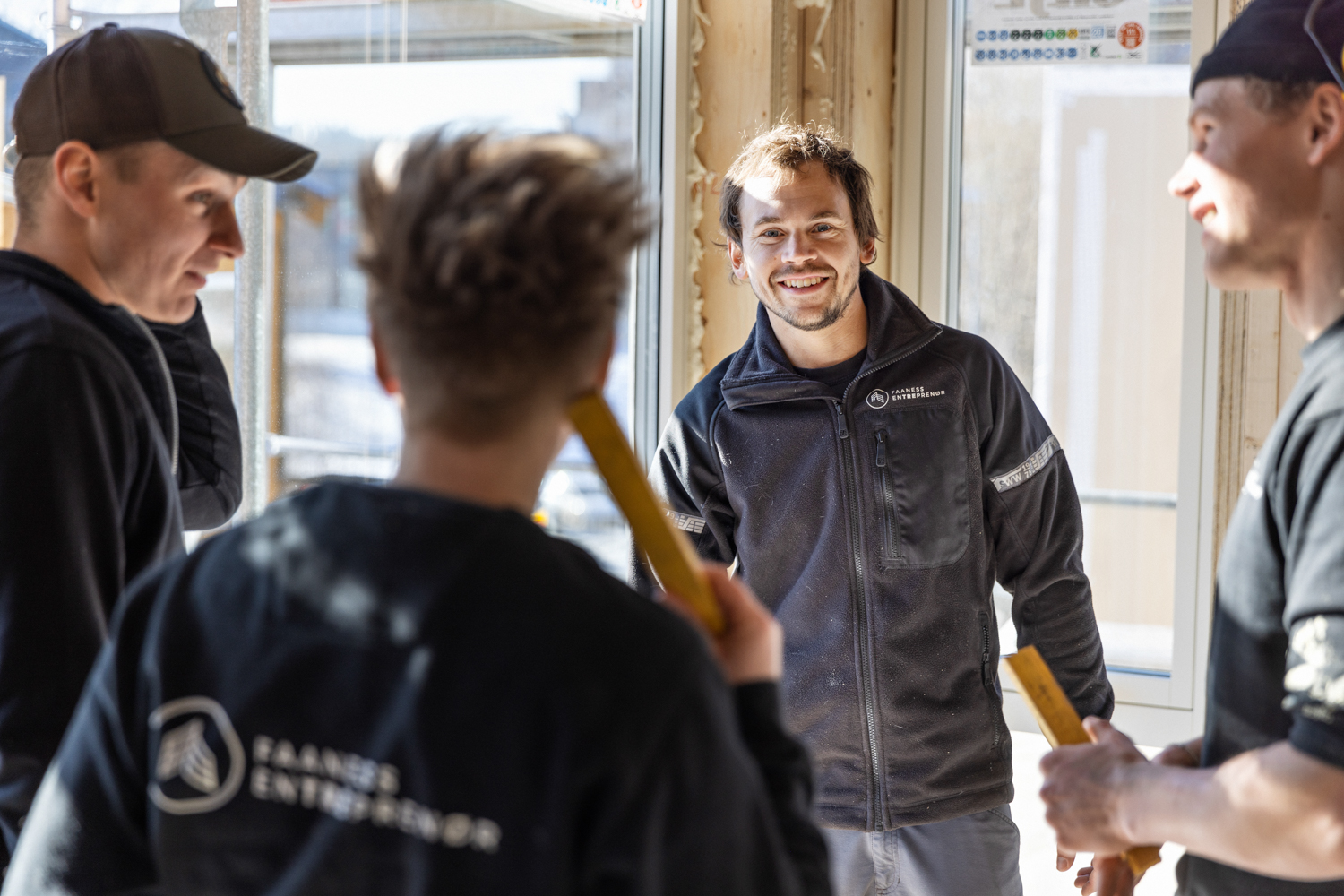 Fire tømrere står å prater sammen i et hus under konstruksjon
