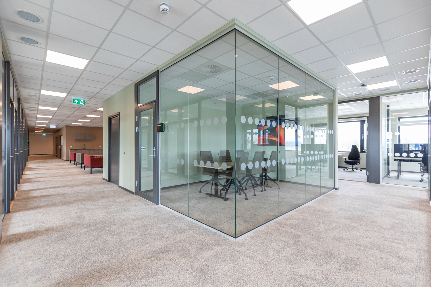 Oversiktsbilde av et lite møterom med glassvegger inne i et større kontorlokale