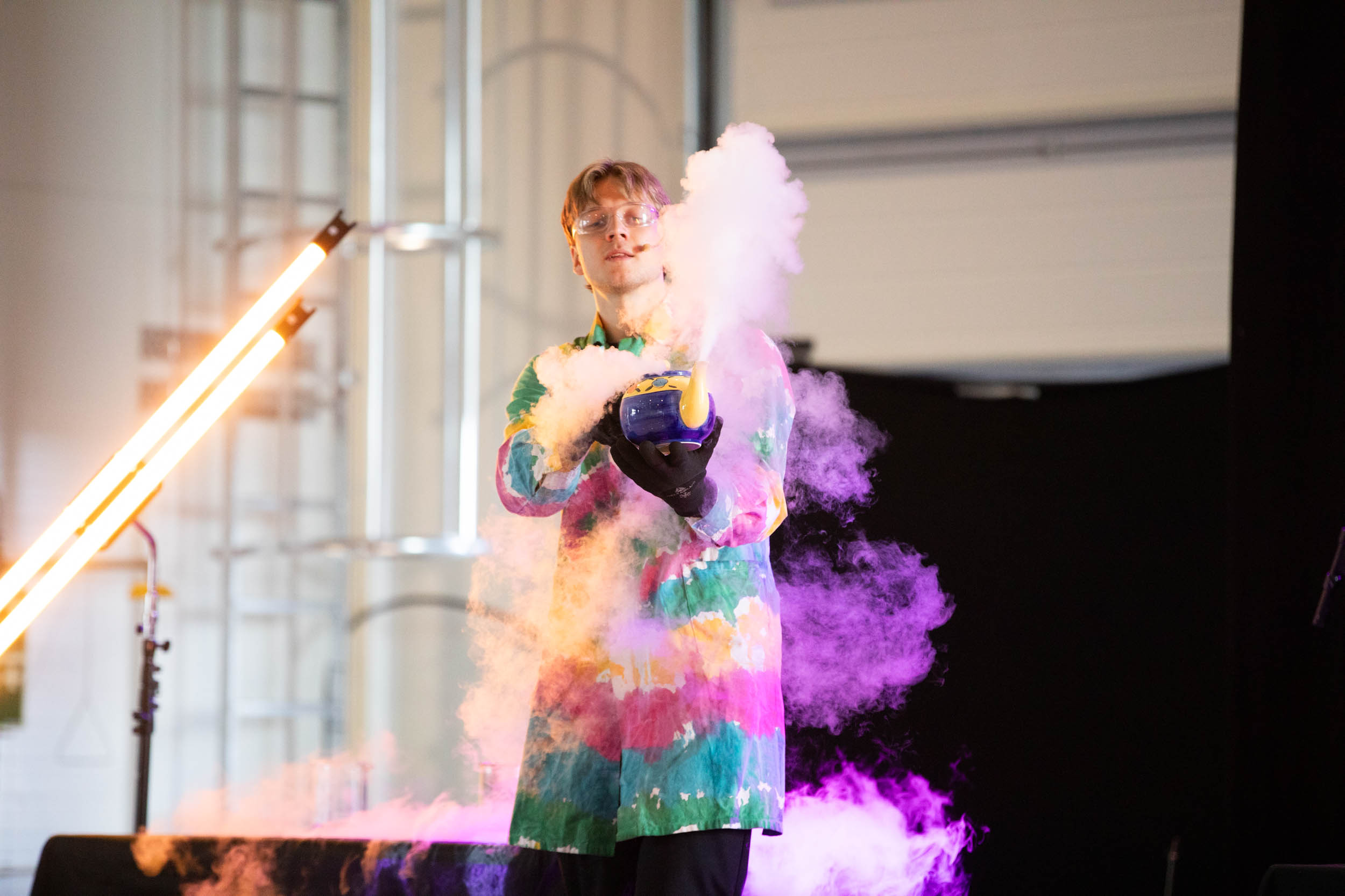 En ung mann står på en scene og lager show med røyk og farger