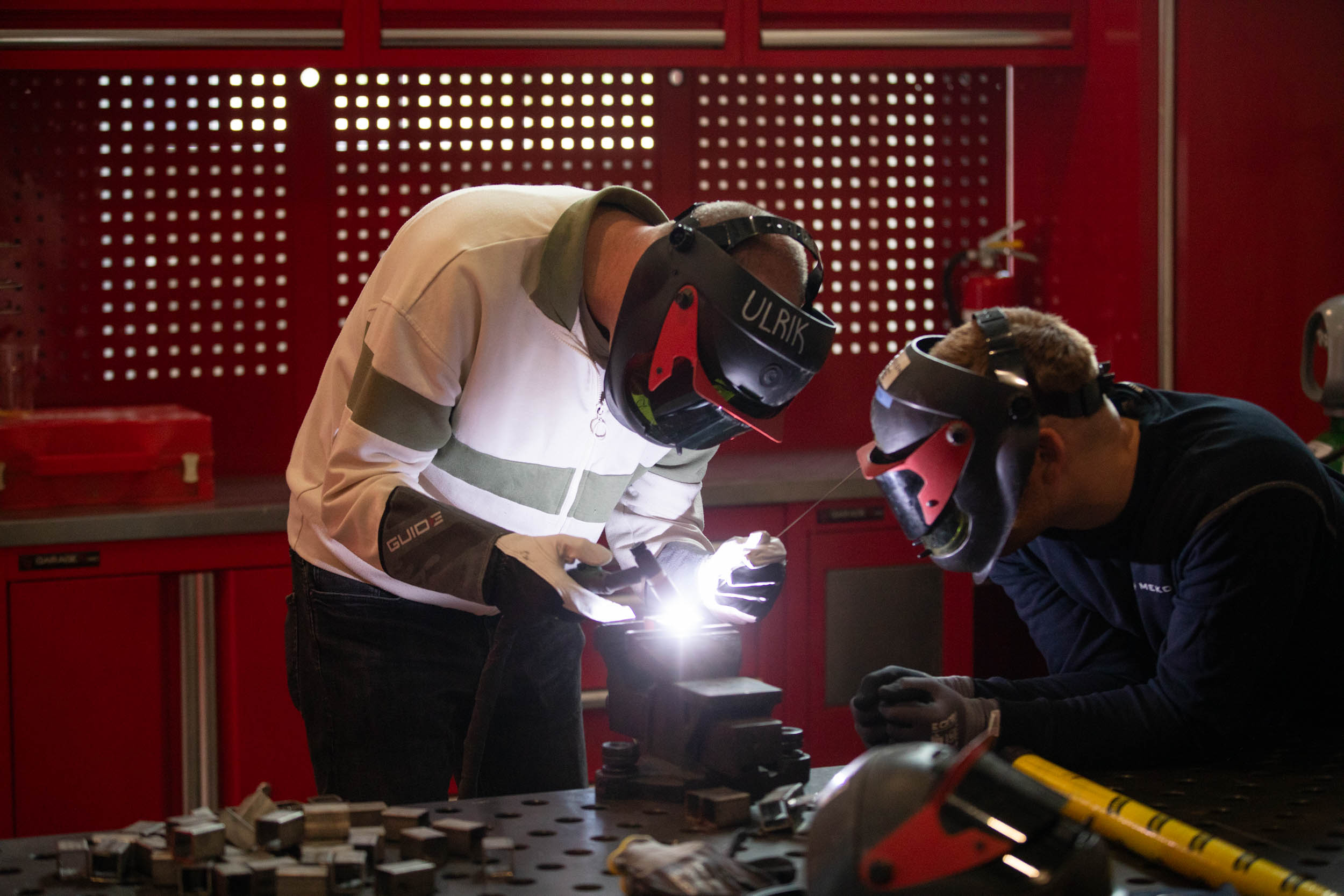 To menn står og sveiser inne på et verksted