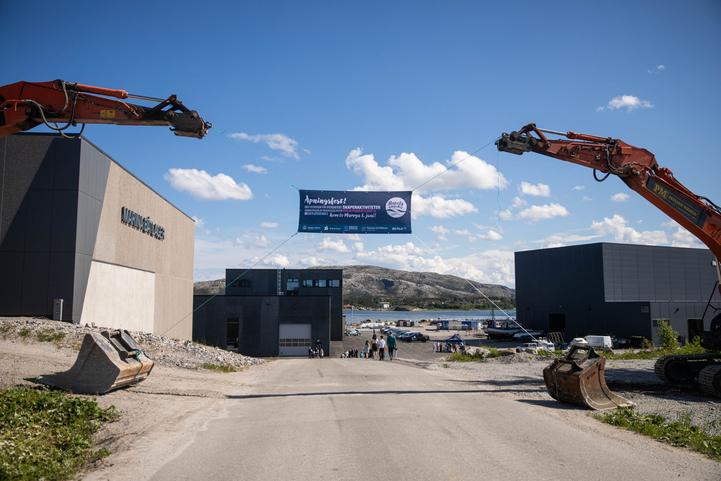 To gravemaskiner holder oppe et skilt festet i tau på et havneområde