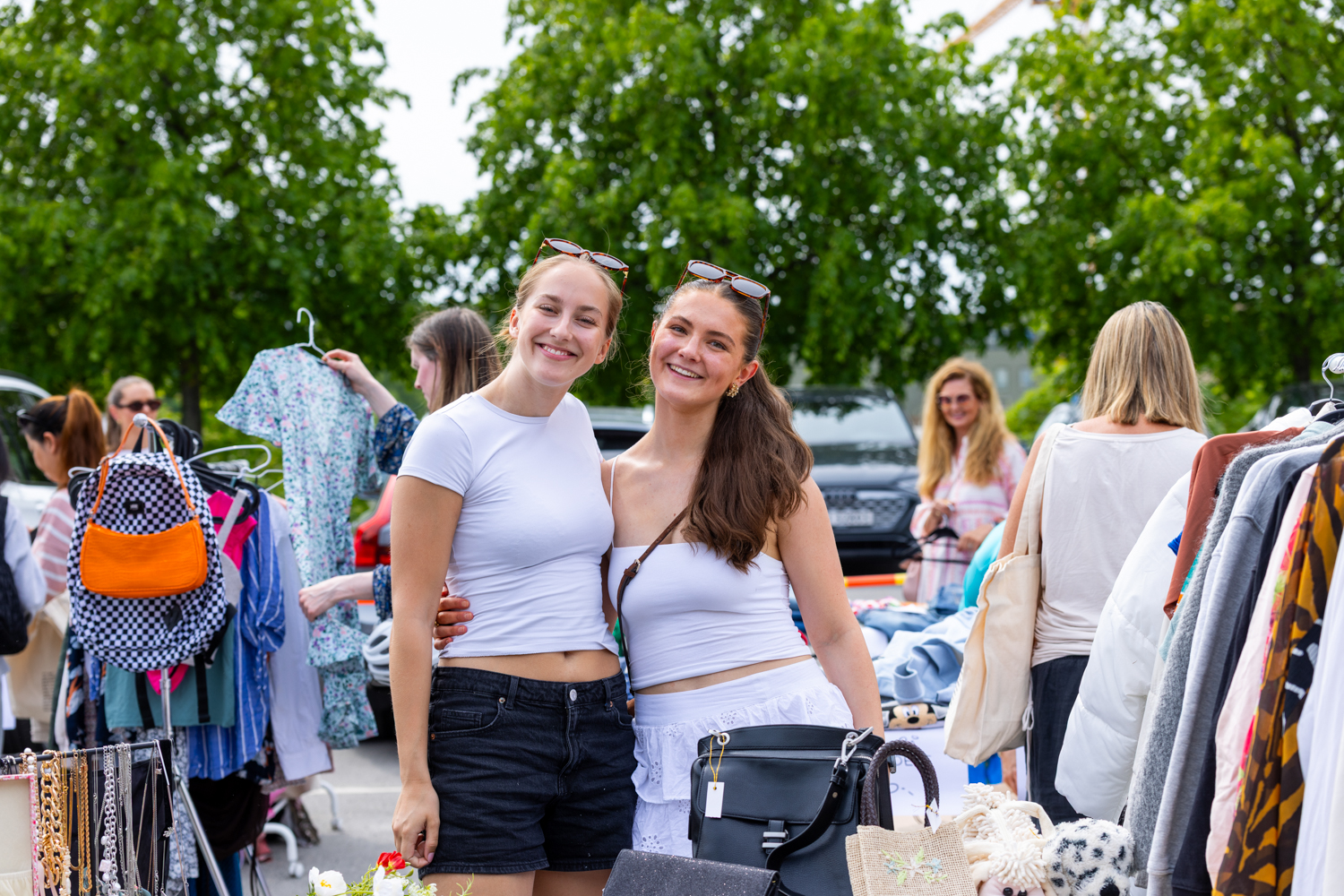 To kvinner smiler til kamera mens de er på et bruktmarked på sommerstid