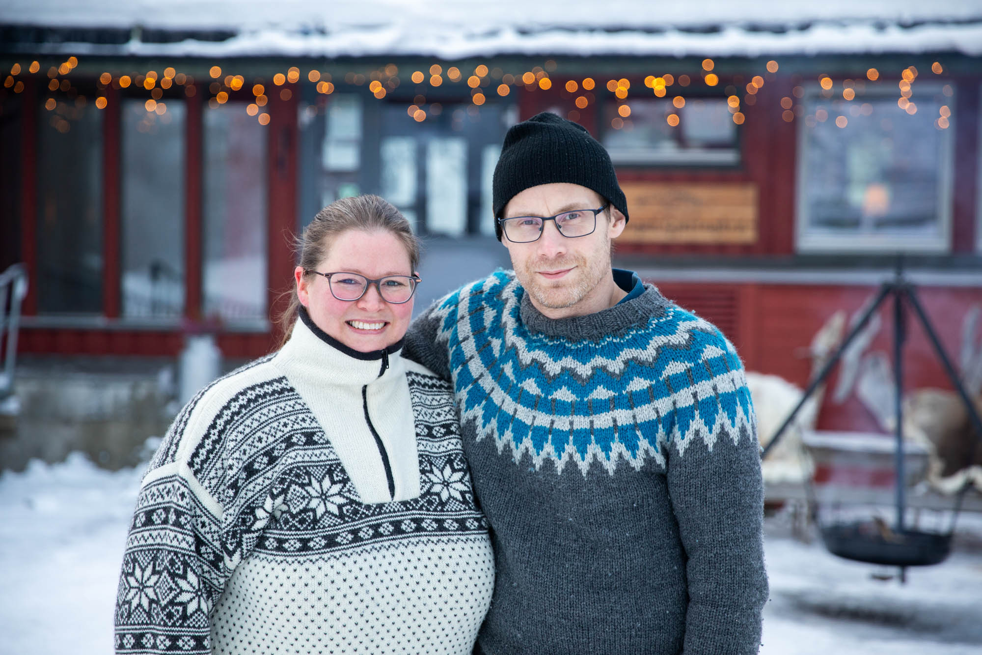 En mann og en kvinne står utenfor en gjestegård ikledd strikkegensere på vinteren