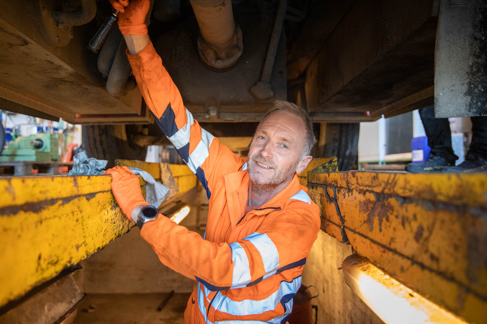 En mann iført arbeidsklær står under en truck og jobber
