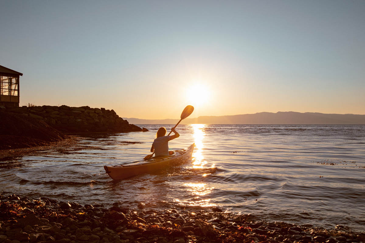 En kvinne som padler i en kajakk i havet mens solen er på vei ned